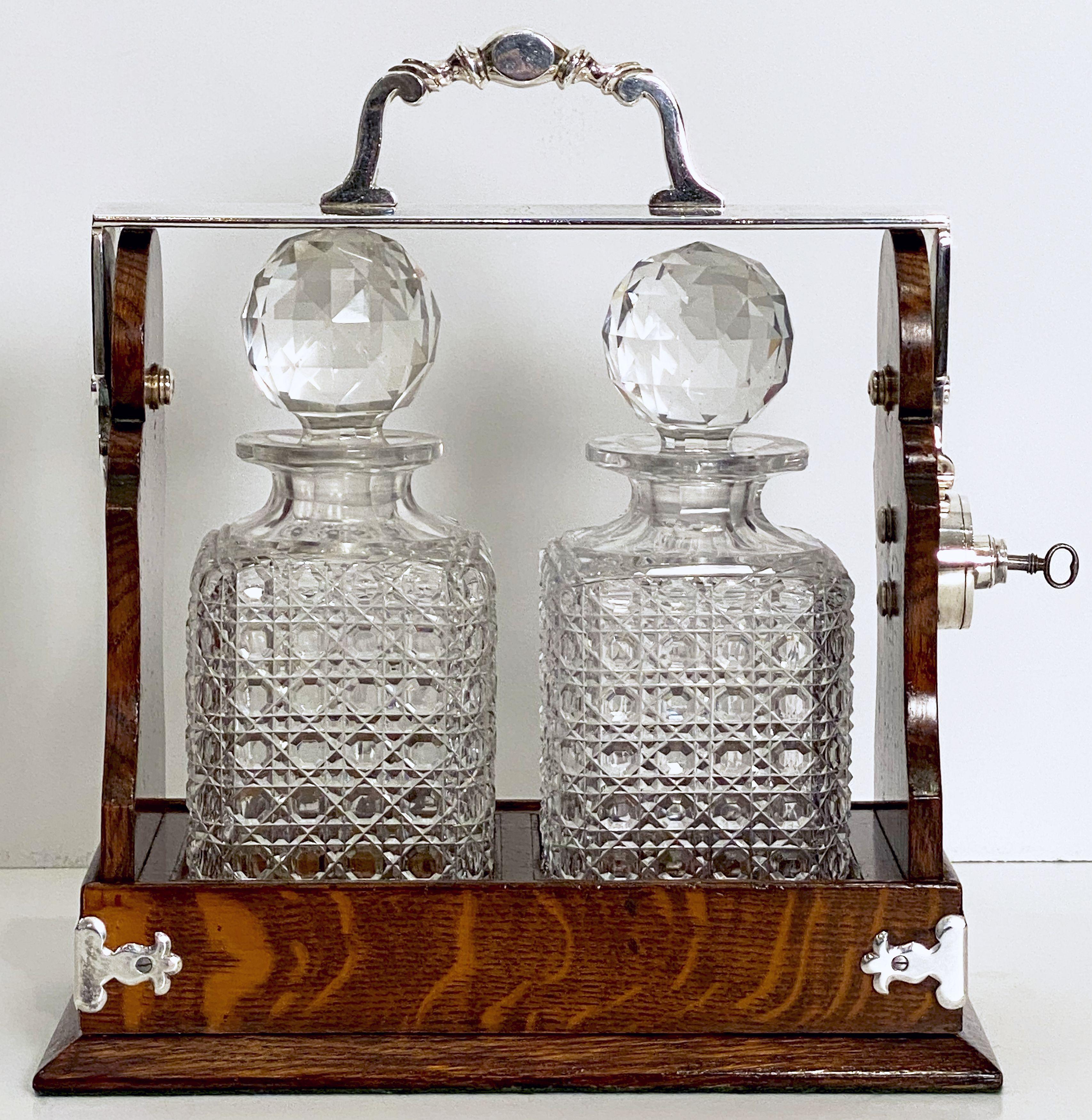 A fine Betjemann's patent tantalus drinks or spirits two-bottle decanter set of oak and silver from Edwardian era England

The tantalus has a silver plated handle and locking mechanism, the hobnail decanters are square in shape and heavily cut