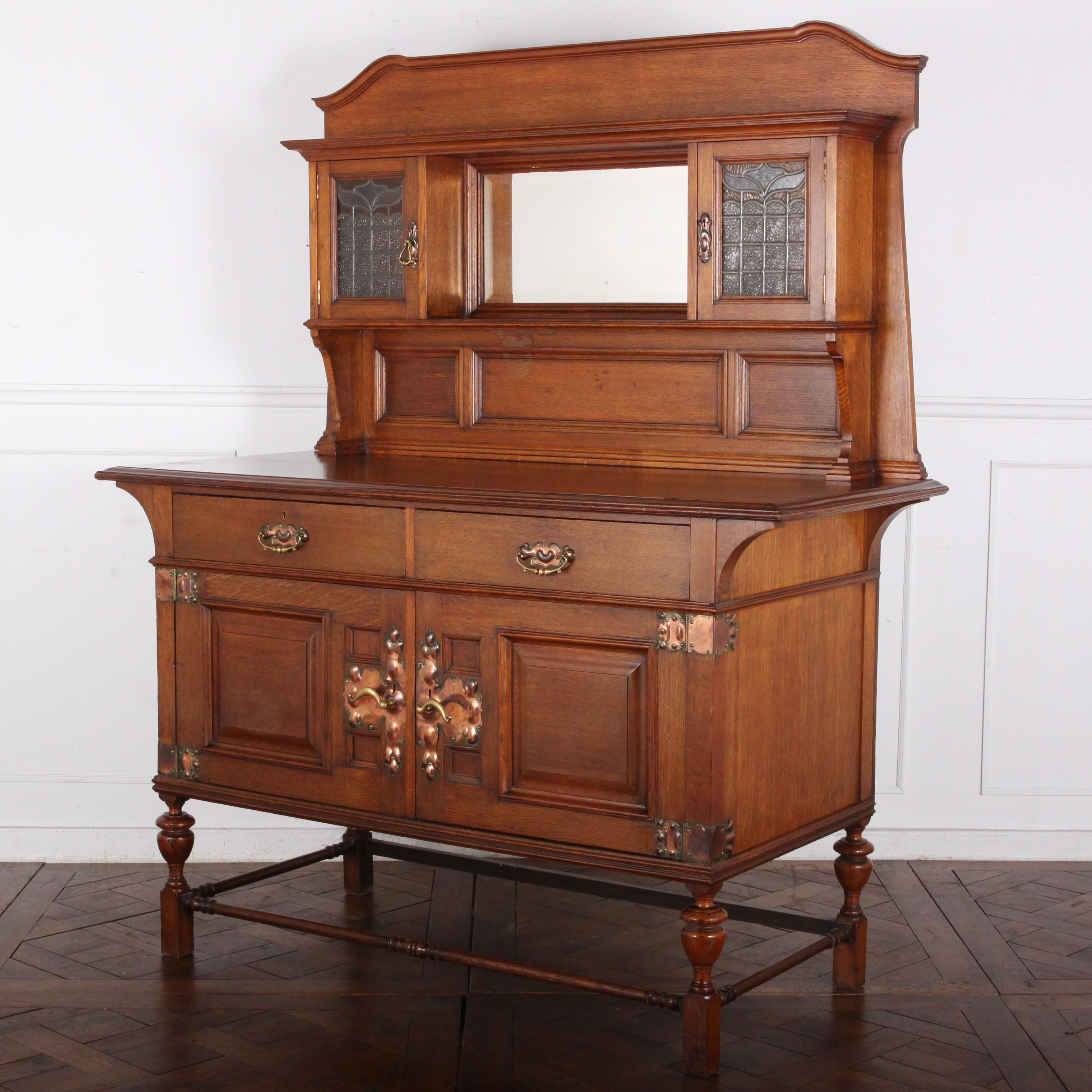 An English Arts & Crafts / Art Nouveau buffet with distinctive copper hardware and leaded-glass upper doors.
A very well-made piece with solid mahogany as the ‘secondary wood’ and handcut joinery throughout.
Signed ‘Maple and Company’.

  