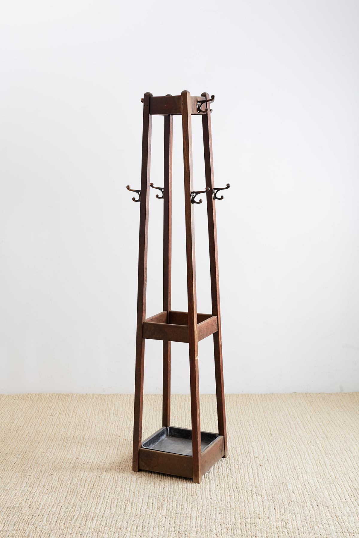 Distinctive English Arts & Crafts hall tree or coat rack featuring a tall tapered oak frame. 8 coat hooks with 4 tall and 4 lower. The bottom of the tree has an umbrella stand with a zinc basin. Unique open design and profile with minimal
