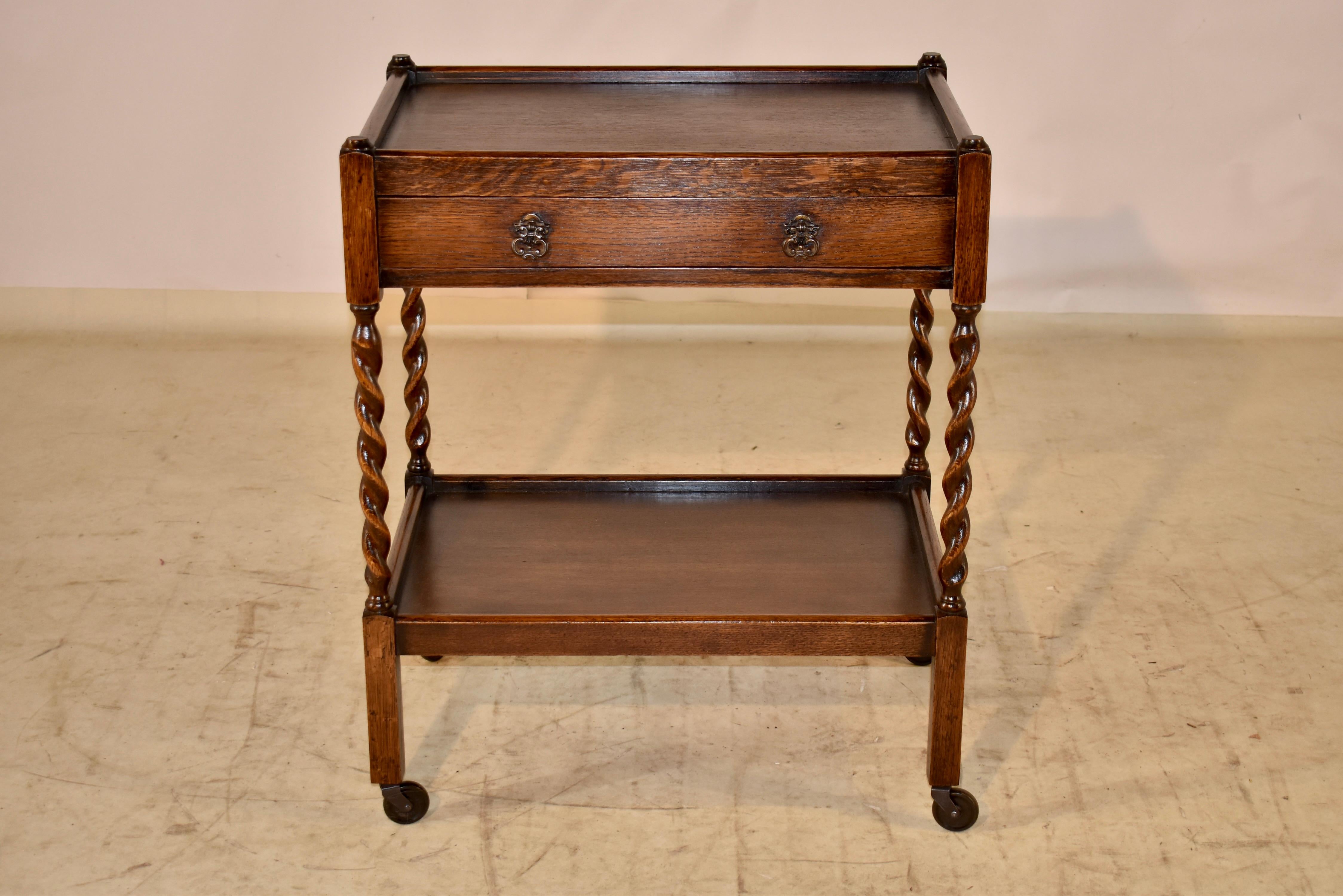Period Edwardian oak bar cart from England. The cart features a top shelf which has a gallery surrounding the edges and follows down to a simple apron, and has a single drawer. The piece is supported on hand turned barley twist legs, joined by a