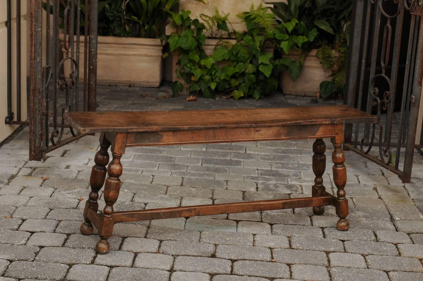 An English oak bench from the mid-19th century, with splayed turned legs and cross stretcher. This English oak bench features a rectangular seat, adorned on the sides with notched motifs. This wooden seat is raised on an exquisite base, comprising