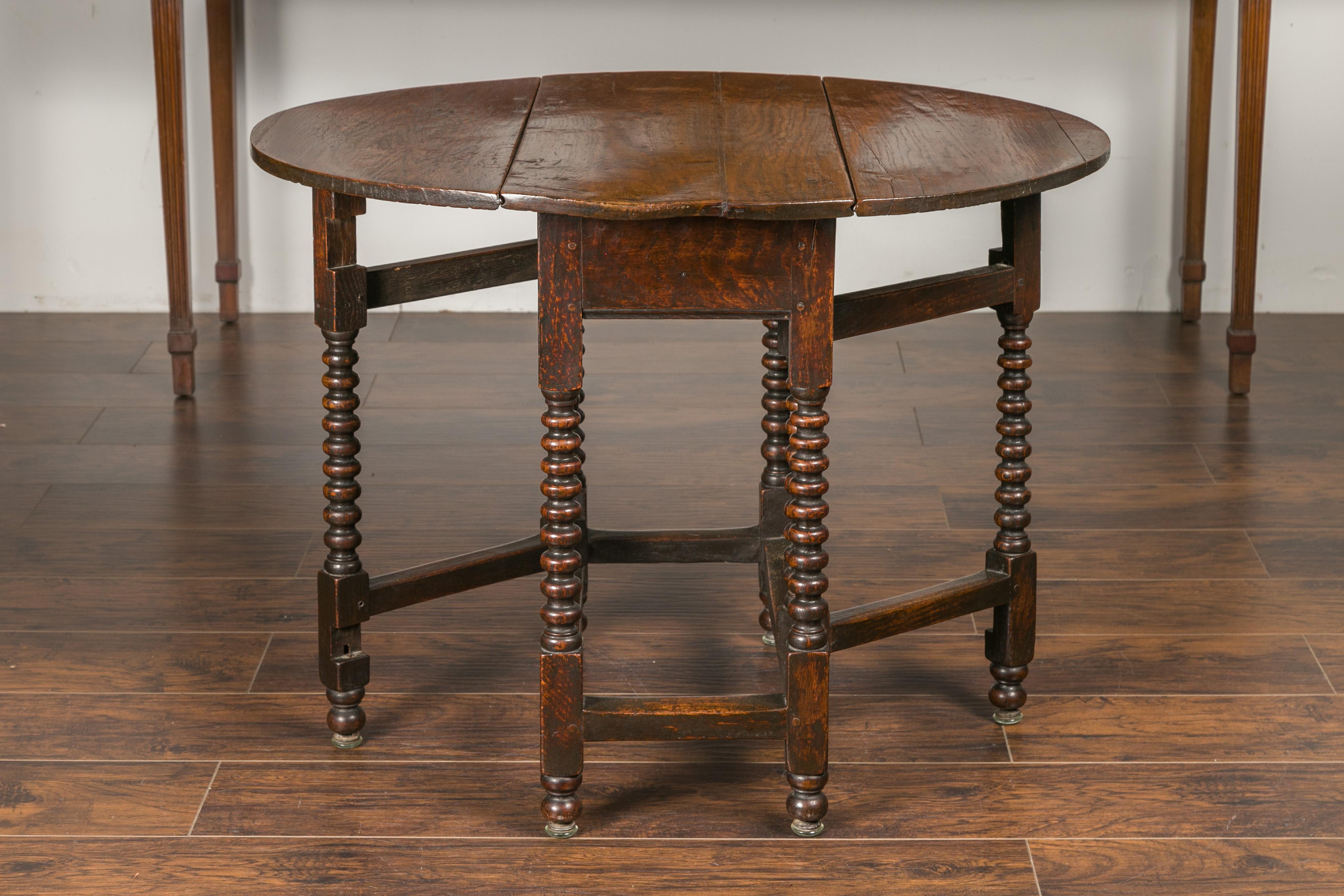 An English oak bobbin leg drop-leaf oval table from the late 19th century, with long drawer and side stretchers. Created in England during the third quarter of the 19th century, this oak table features an oval top made of two drop leaves resting on