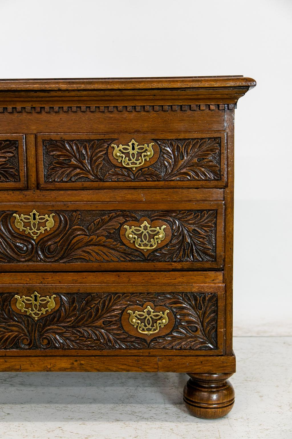 English Oak Carved Four Drawer Chest, has a dentil cornice and frieze. The drawers depict carved leaves and other foliate patterns. It retains one of its original locks for the top right hand drawer.