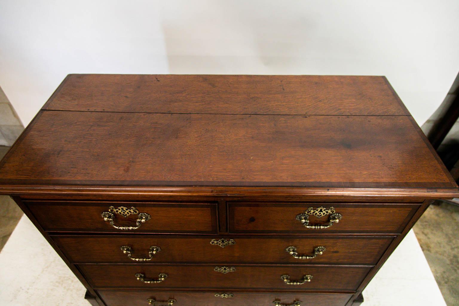 The top of this chest of drawers has an ogee molded edge and is crossbanded with mahogany. The drawer fronts also are crossbanded with mahogany and have antique hardware that is not original. The corners have fluted quarter columns that terminate in