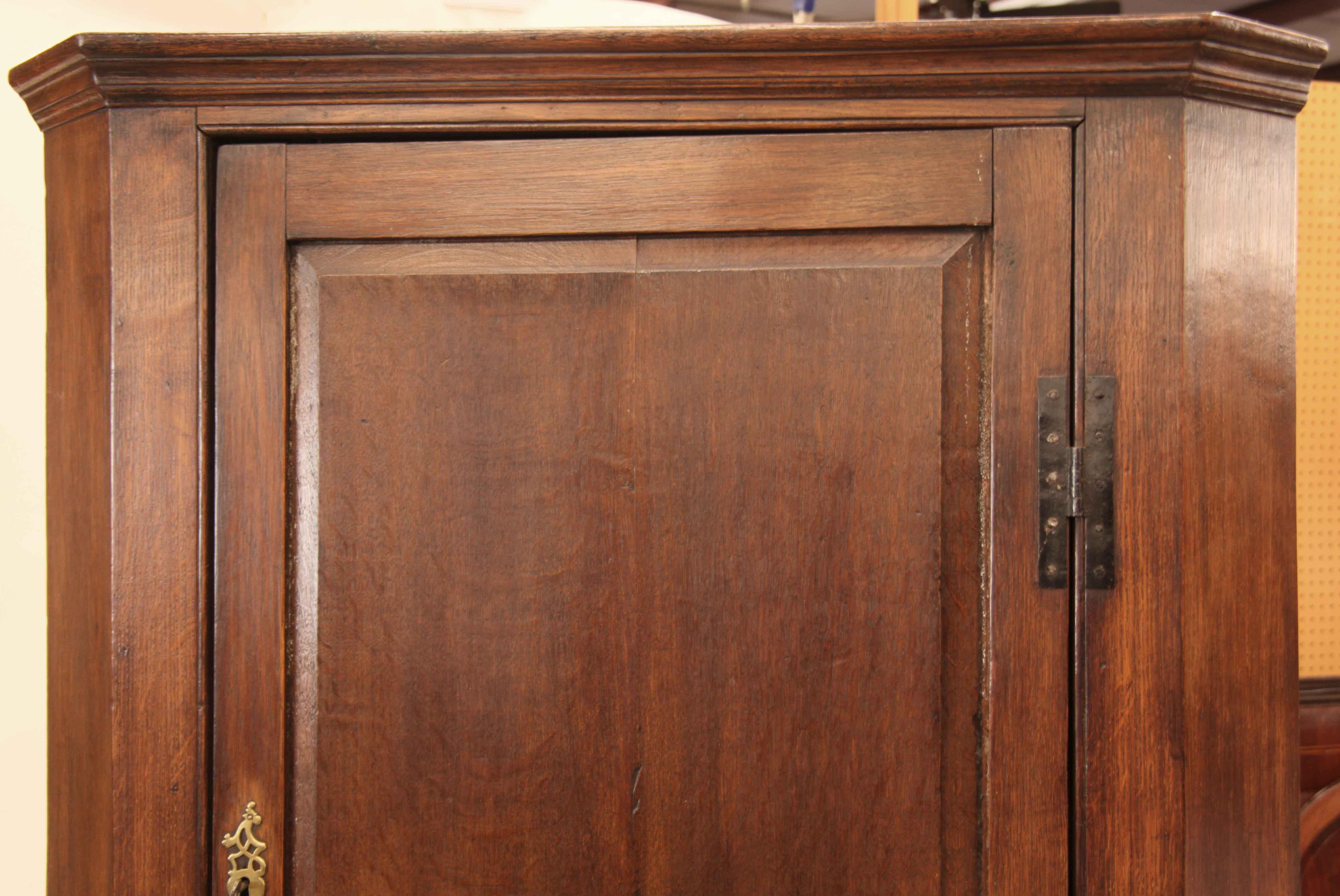 English oak corner cupboard, the cove cornice above large raised panel door (and smaller door below) with steel ''H'' hinges, reticulated brass escutcheons; both doors with working locks and keys. Upper and lower interiors with shelves and  grain