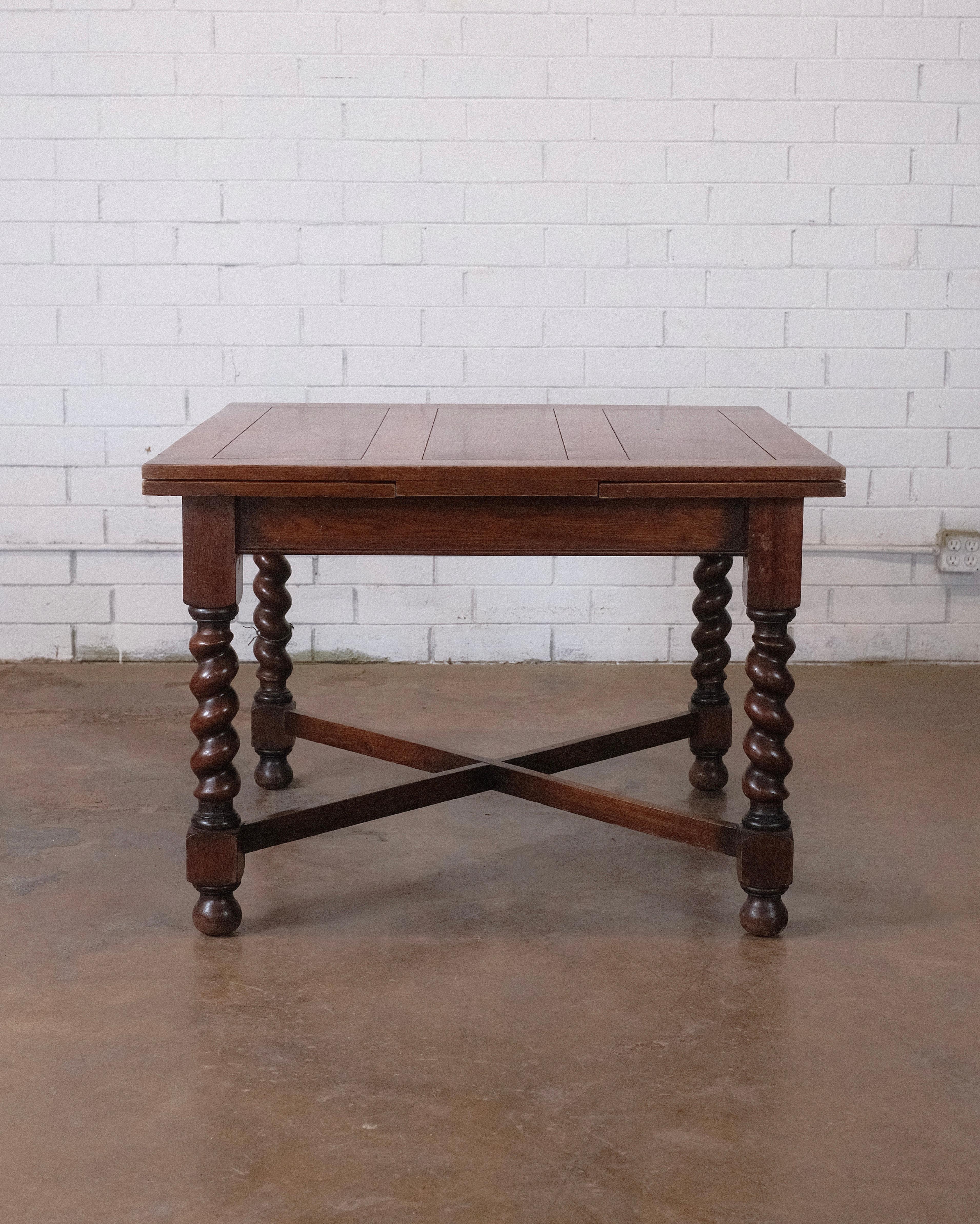 Presenting an Edwardian oak pub table from circa 1900, featuring convenient draw leaves for adaptable seating. The top and leaves boast paneled detailing, supported by a straightforward apron that gracefully descends to hand-turned barley twist