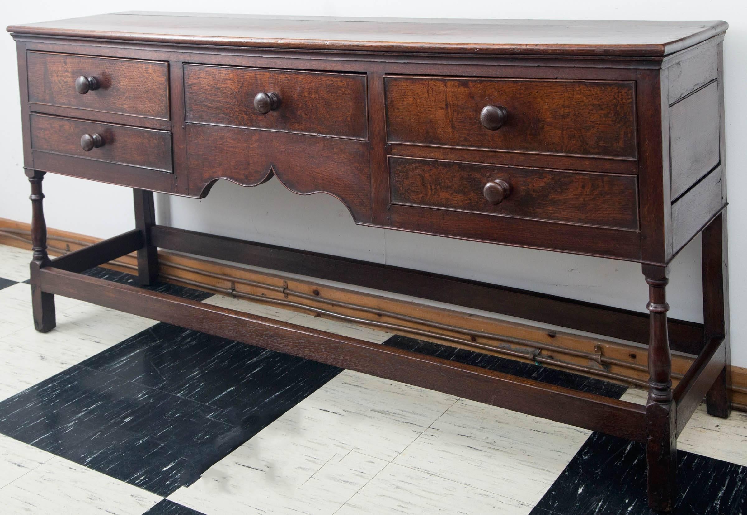 English oak five-drawer dresser base with elegant arched central apron. Dresser rests on turned legs with stretchers. Exceptional color and patina.