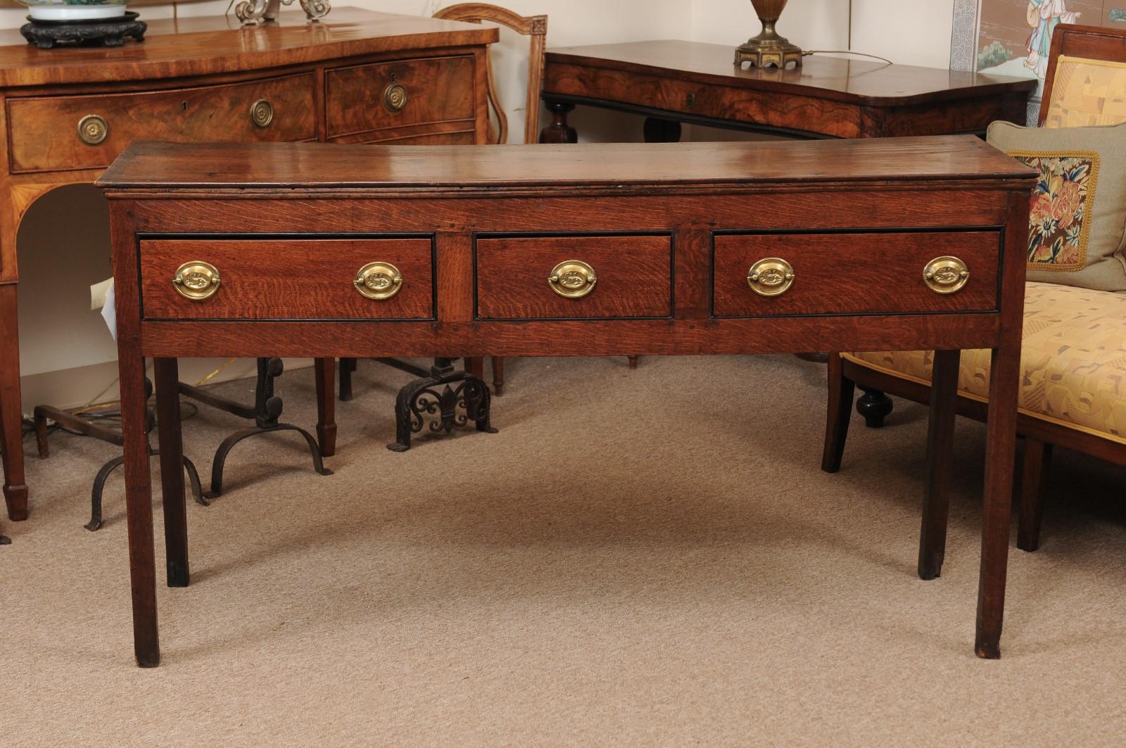 An early 19th century English oak dresser base/server featuring 3 drawers with brass pulls and square legs.