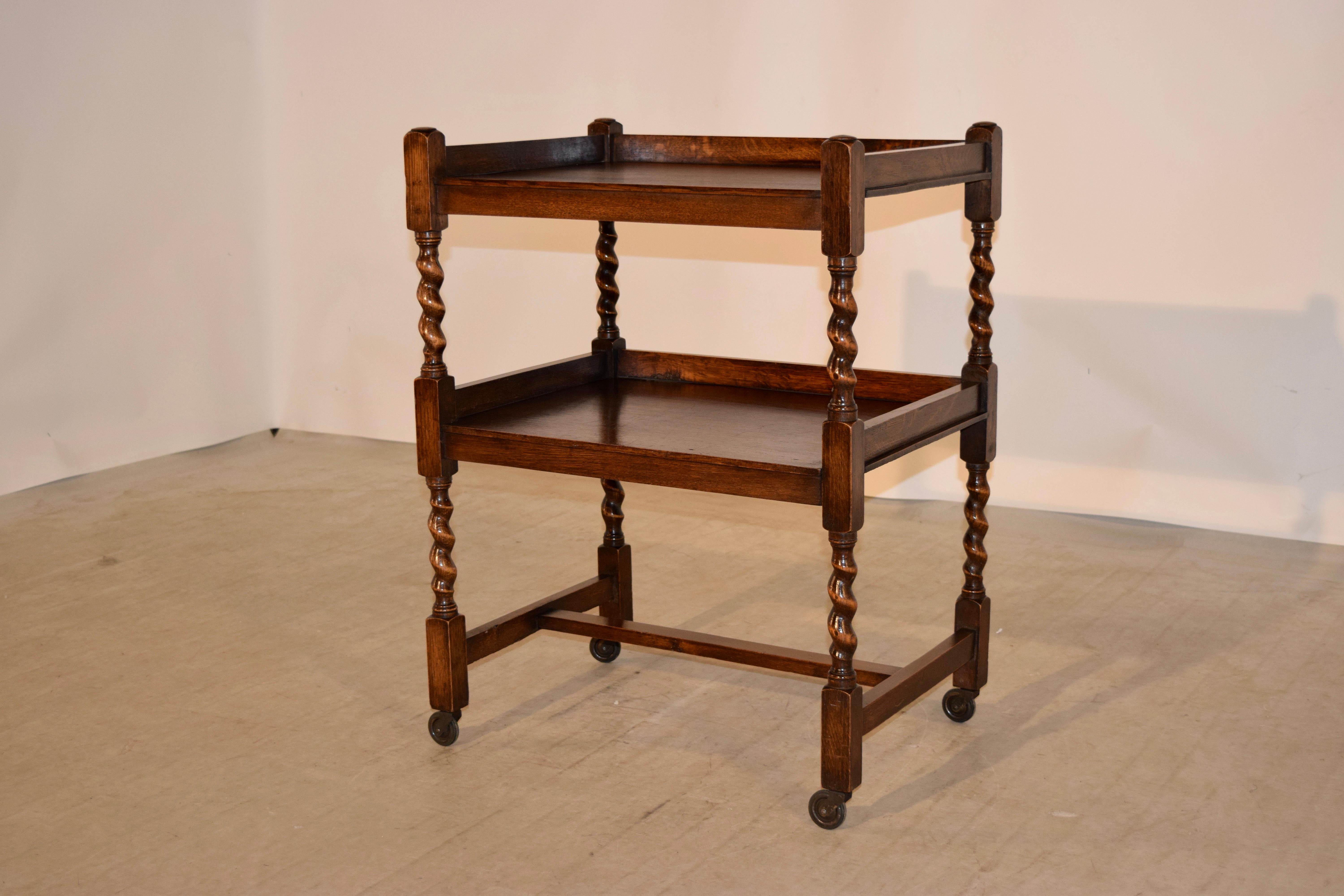 English oak drinks cart with two shelves, both with galleries and separated by hand turned barley twist shelf supports and supported on hand-turned barley twist legs, joined by simple stretchers and raised on original casters.