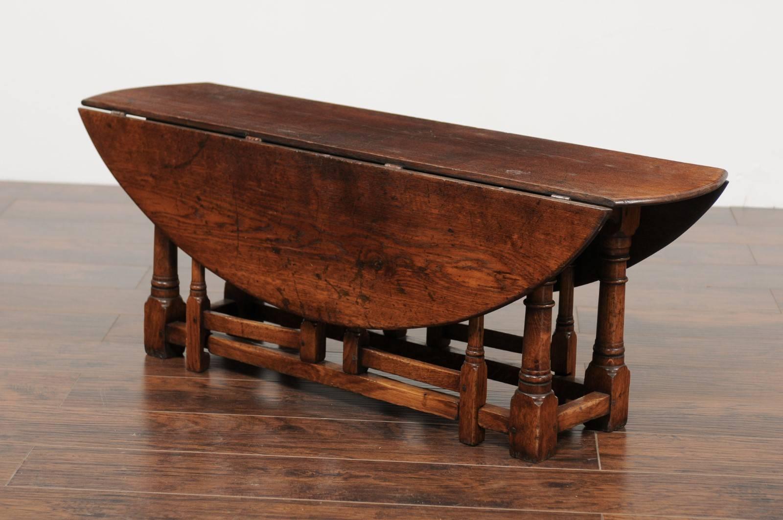 An unusual English oak oval top drop-leaf coffee table with double gateleg from the late 19th century. This English oak table features an oval top made of two drop leaves. The depth of the table when the leaves are down is 12.5