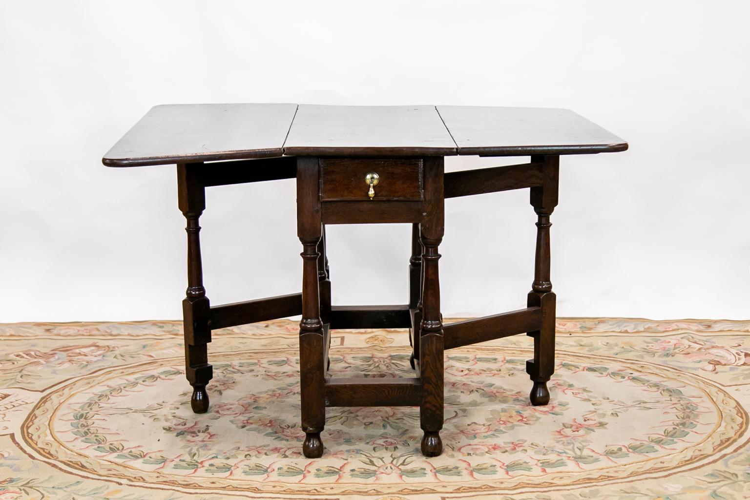 This gate leg table has a drawer with incised thumb nail molding and a brass tear drop pull, which is old but not original. There is exposed peg construction. 
Width of the table closed: 16.25