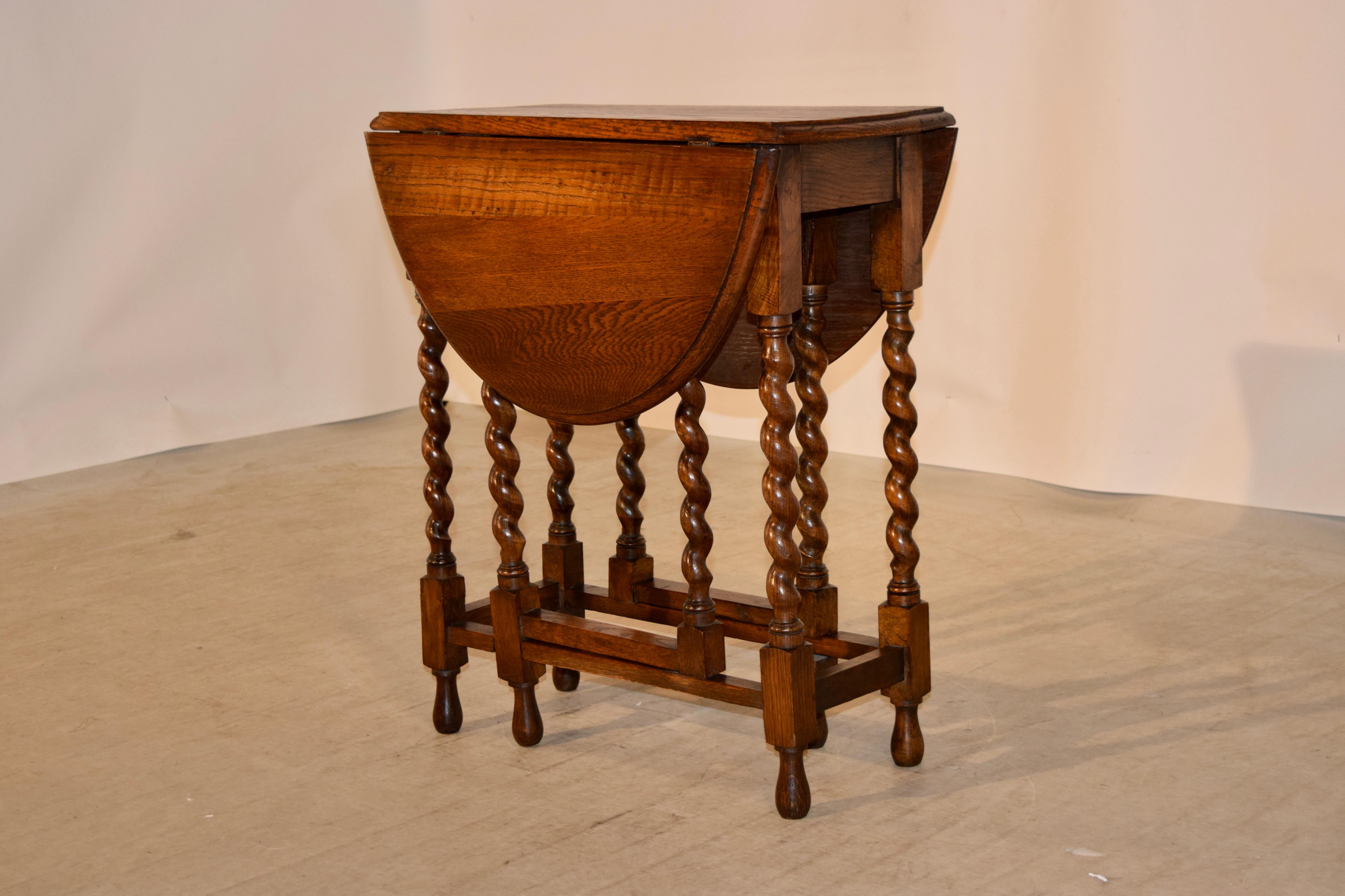 English oak gate leg table with a bevelled edge around the top, following down to a simple apron and supported on hand-turned barley twist legs and gates. There are simple stretchers connecting the legs and base and the table is raised on