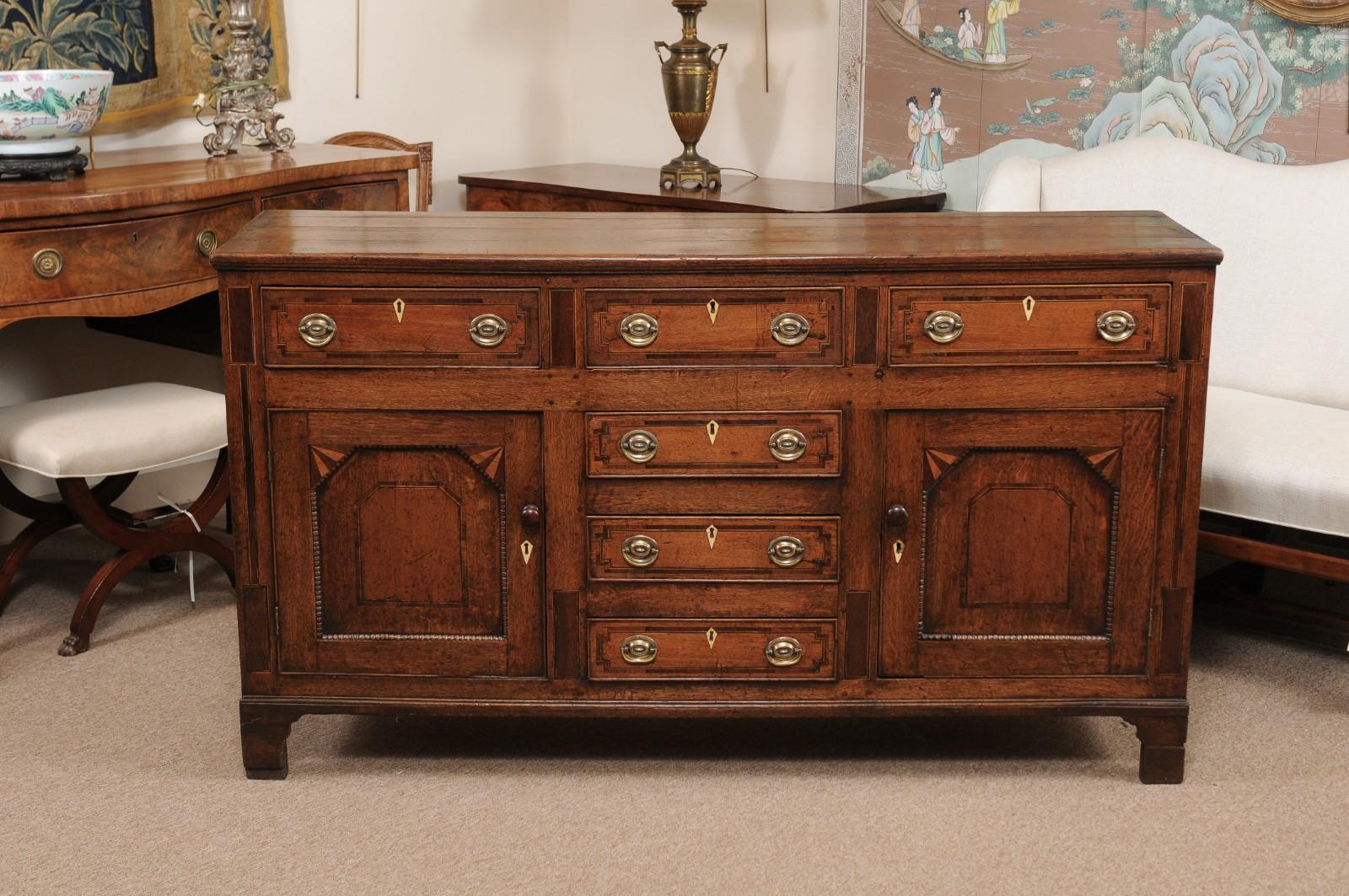 The English oak George III dresser base with shallow rectangular top, 6 drawers and 2 flanking side paneled cabinets with ebonized and boxwood string inlay ending in bracket feet.