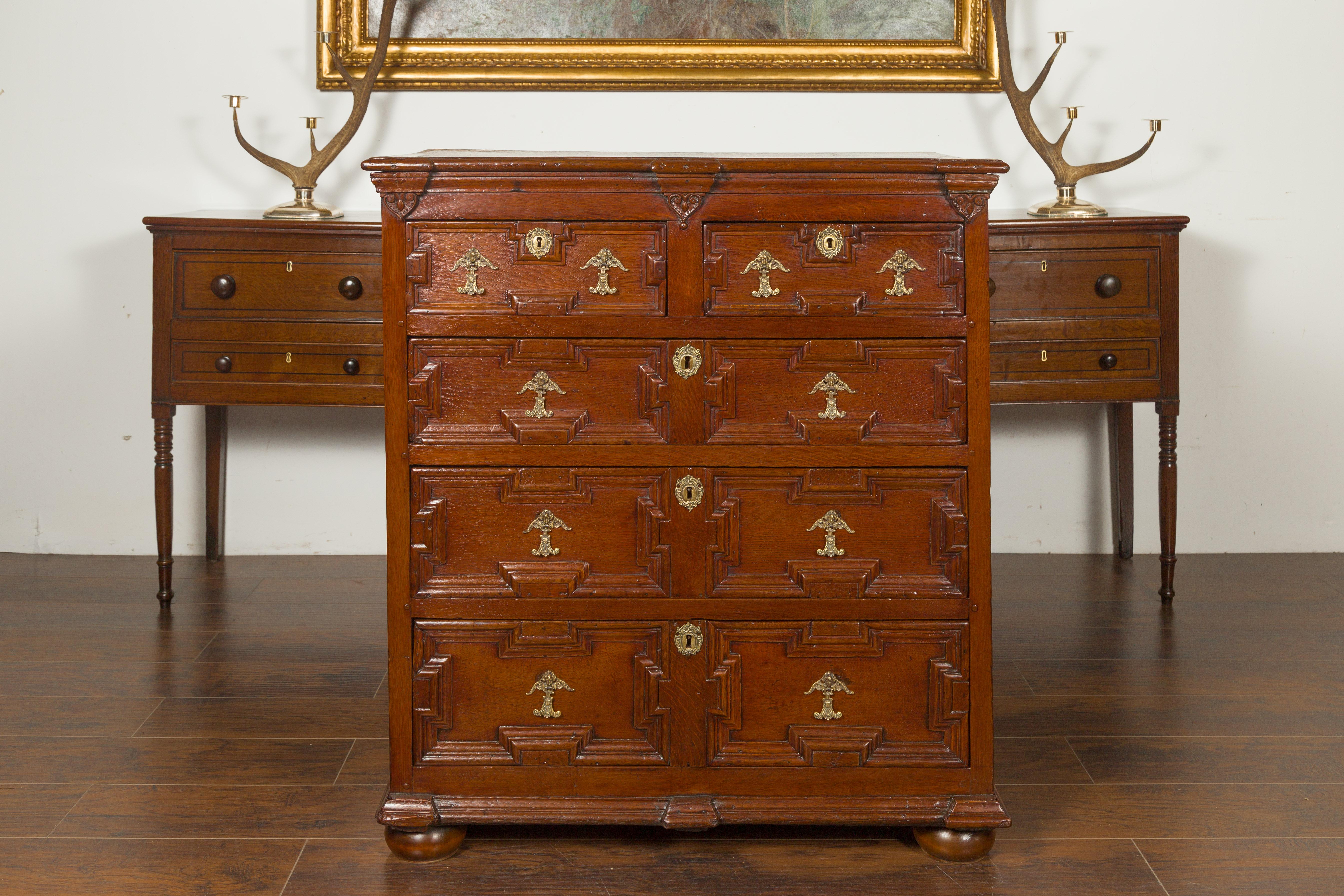 An English oak Georgian period geometric front five-drawer chest from the early 19th century, with heart motifs and ornate hardware. Born in England during the early years of the 19th century, this oak chest features a rectangular top with