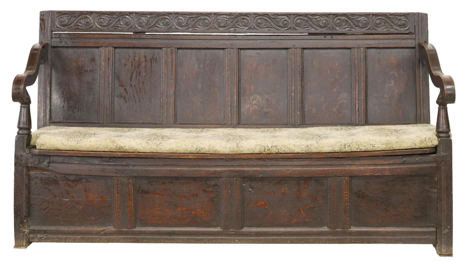 English oak settle hall bench, 18th c. This bench features scrolling foliate carved crest, over paneled back, curved arms on turned supports, removable seat cushion above hinged seat, opening to interior storage, rising on conforming base, some wood