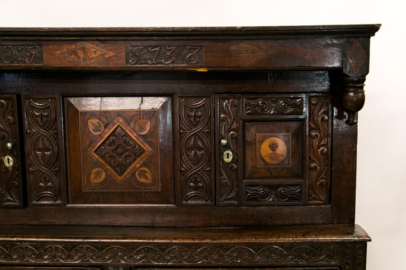 This court cupboard has protruding free standing carved pendants on the top. The upper doors have raised panels inlaid with satinwood and ebony figures of stylized knights. The center panels of the upper half and two lower doors are inlaid with