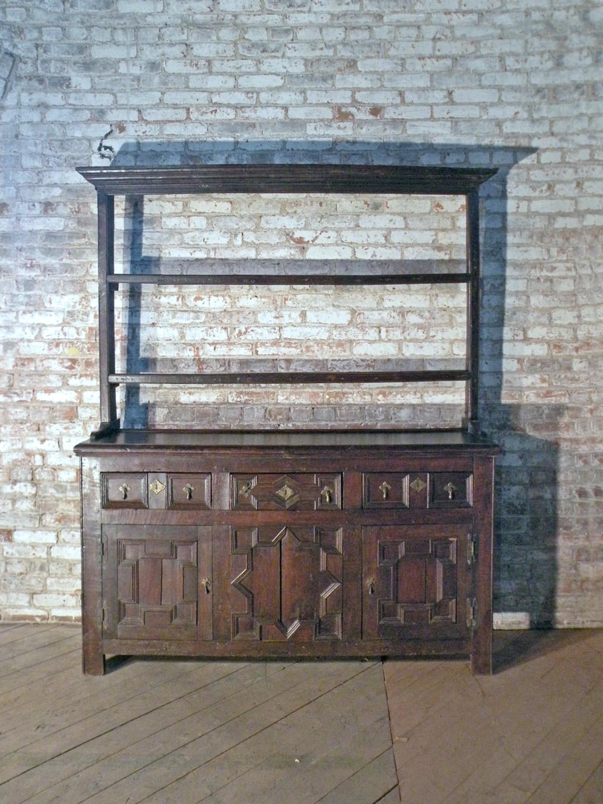 Buffet / Cupboard / Dresser - of unusual narrow proportions. The lower cabinet part having three drawers over two beautifully geometrically paneled doors flanking a stationary conforming middle panel, the interior with one continuous shelf. The