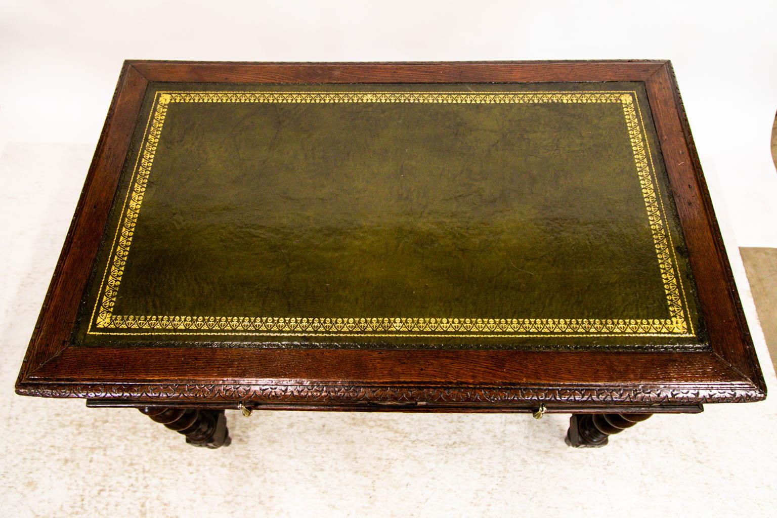 This English writing table is made of beautiful oakwood. The leather top is a deep olive with gold detailing around the edges. The top edge of this writing table is carved with stylized inverted arches.