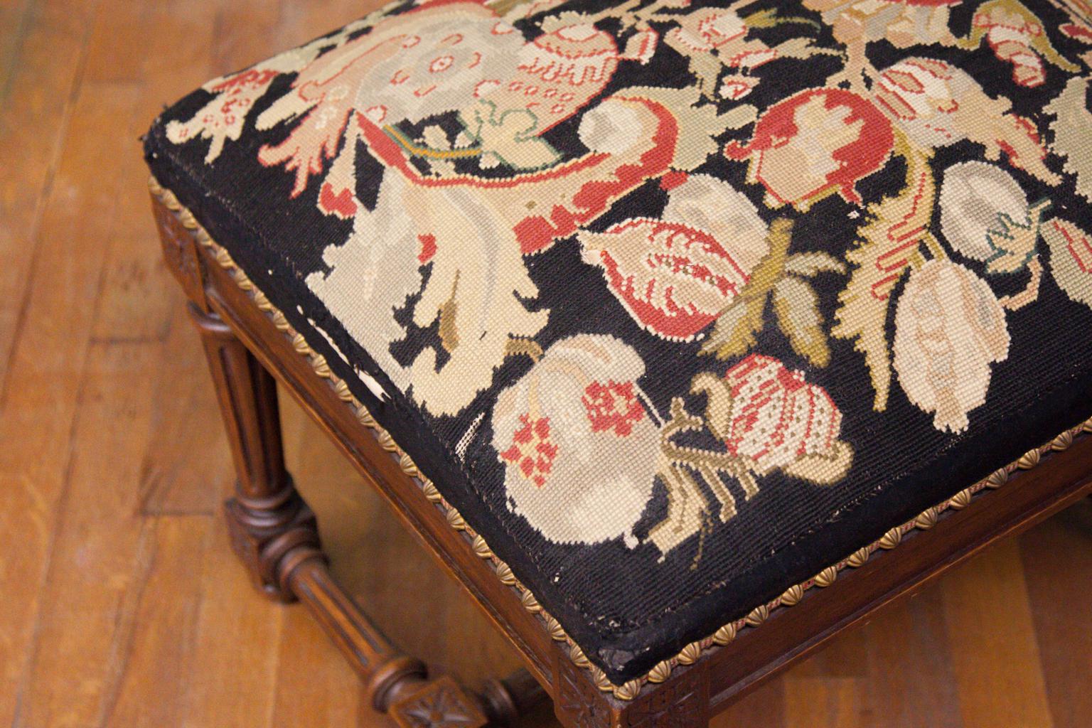 English oak needlework stool, with tapered fluted legs and a turned finial on the cross stretcher. There are square carved floral rosettes on the legs and stretcher. The upholstery has faceted brass stud work. Note that there is some deterioration