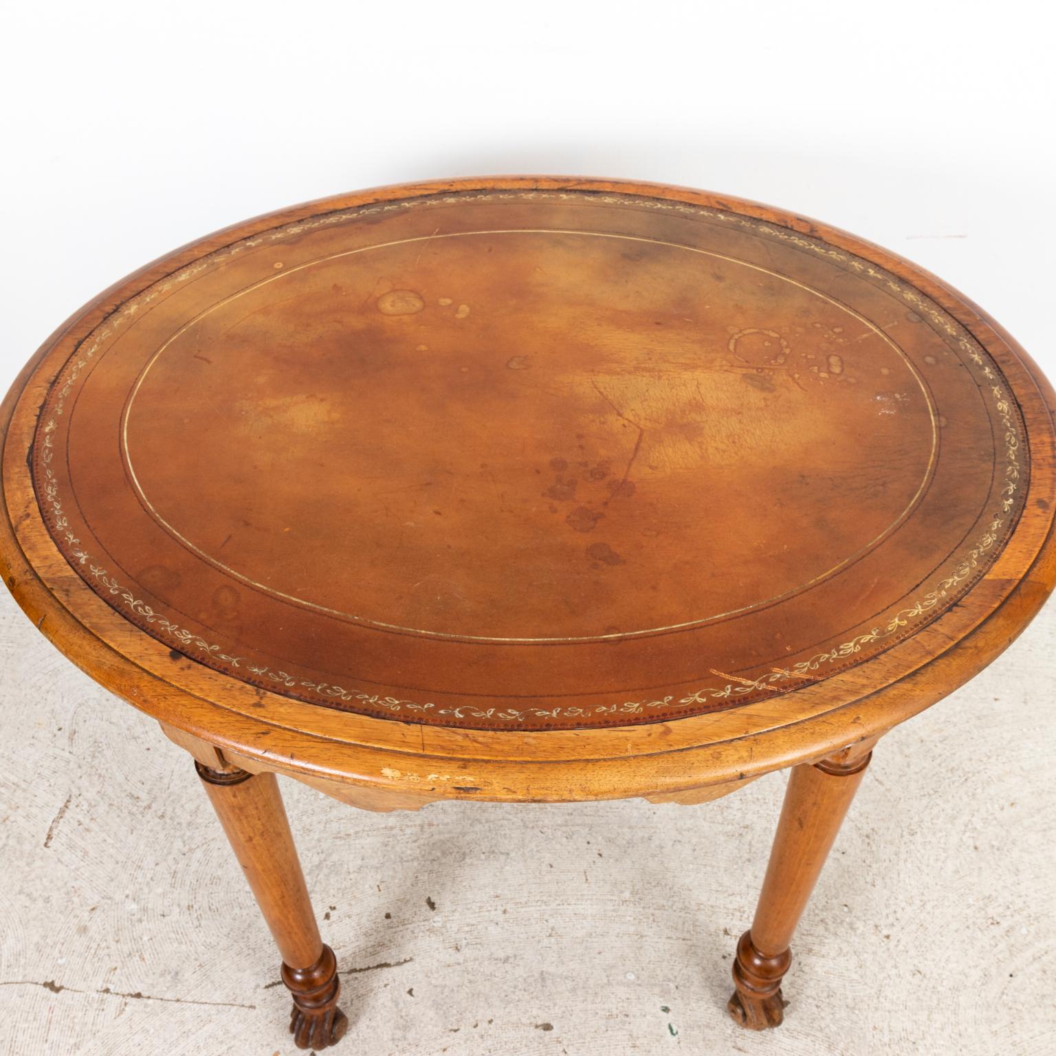 Circa 1920s English oval oakwood table with foliage trim on the embossed leather top. The table also featured a curved apron, ball turned legs, and Flemish scroll feet. Made in England. Please note of wear consistent with age including finish loss