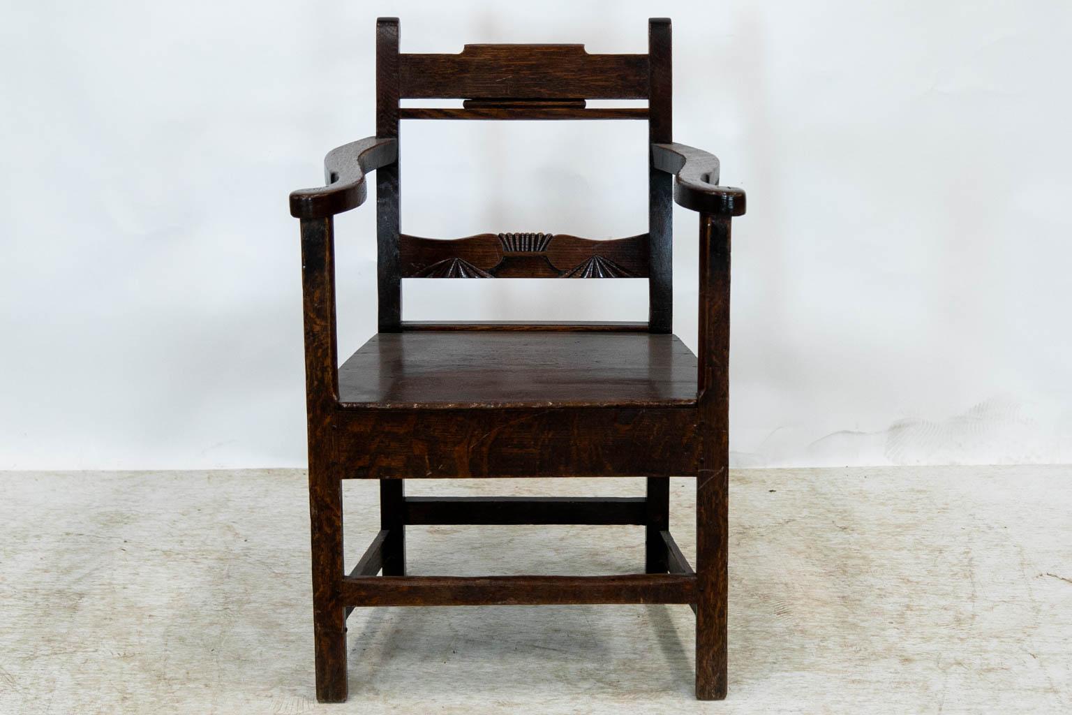 This armchair has exposed peg construction. The back has a lower support that is carved with reeded fans. The legs are joined by perimeter stretchers.