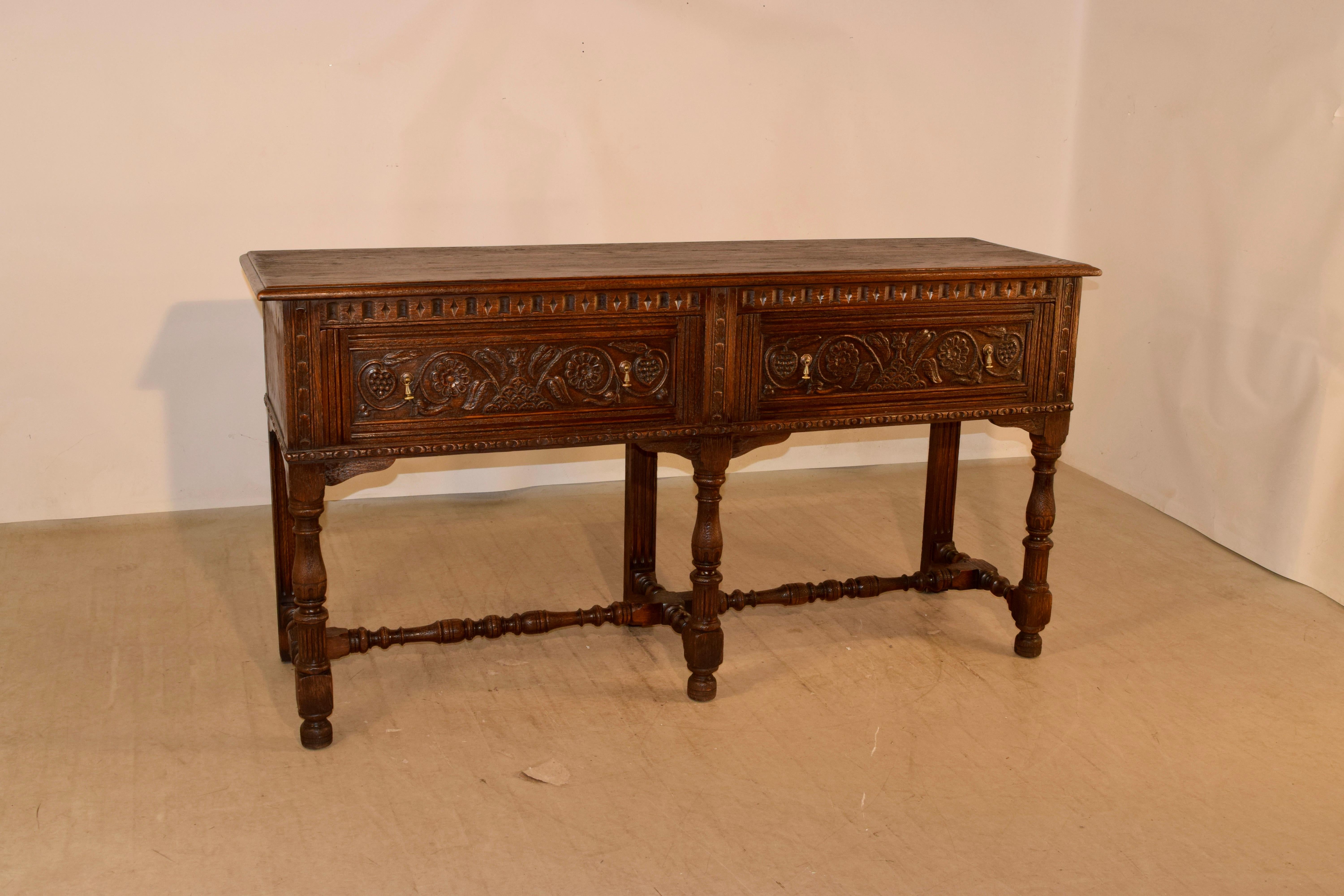 English oak sideboard, circa 1920. The top has a beveled edge and follows down to simple sides and a wonderfully carved case in the front. The front contains two drawers, both with exquisitely carved drawer fronts and supported on hand turned legs