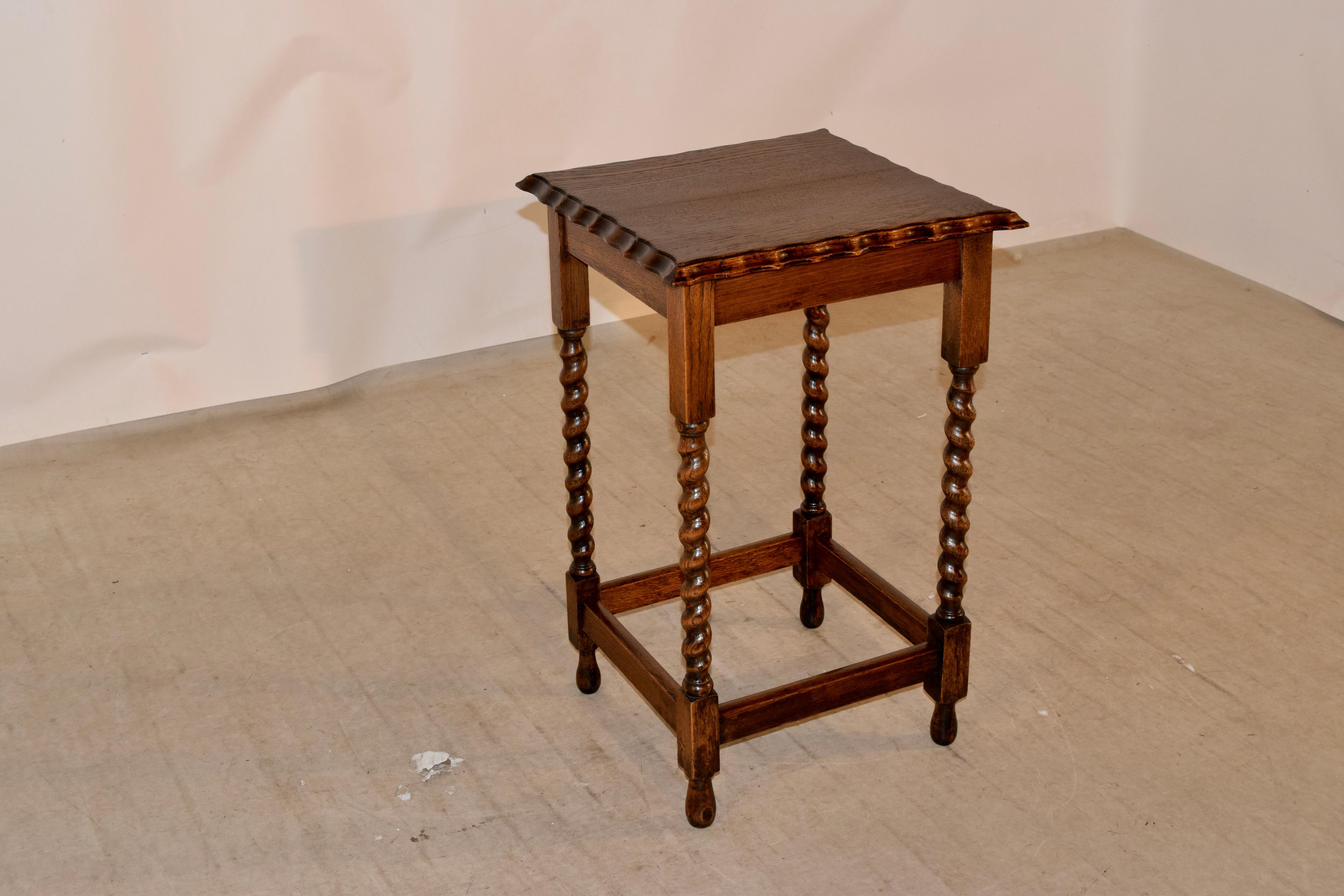 English oak side table with a square top, circa 1900. The top is scalloped and beveled around the edge, following down to a simple apron. The table is supported on hand turned barley twist legs, joined by simple stretchers and raised on hand turned