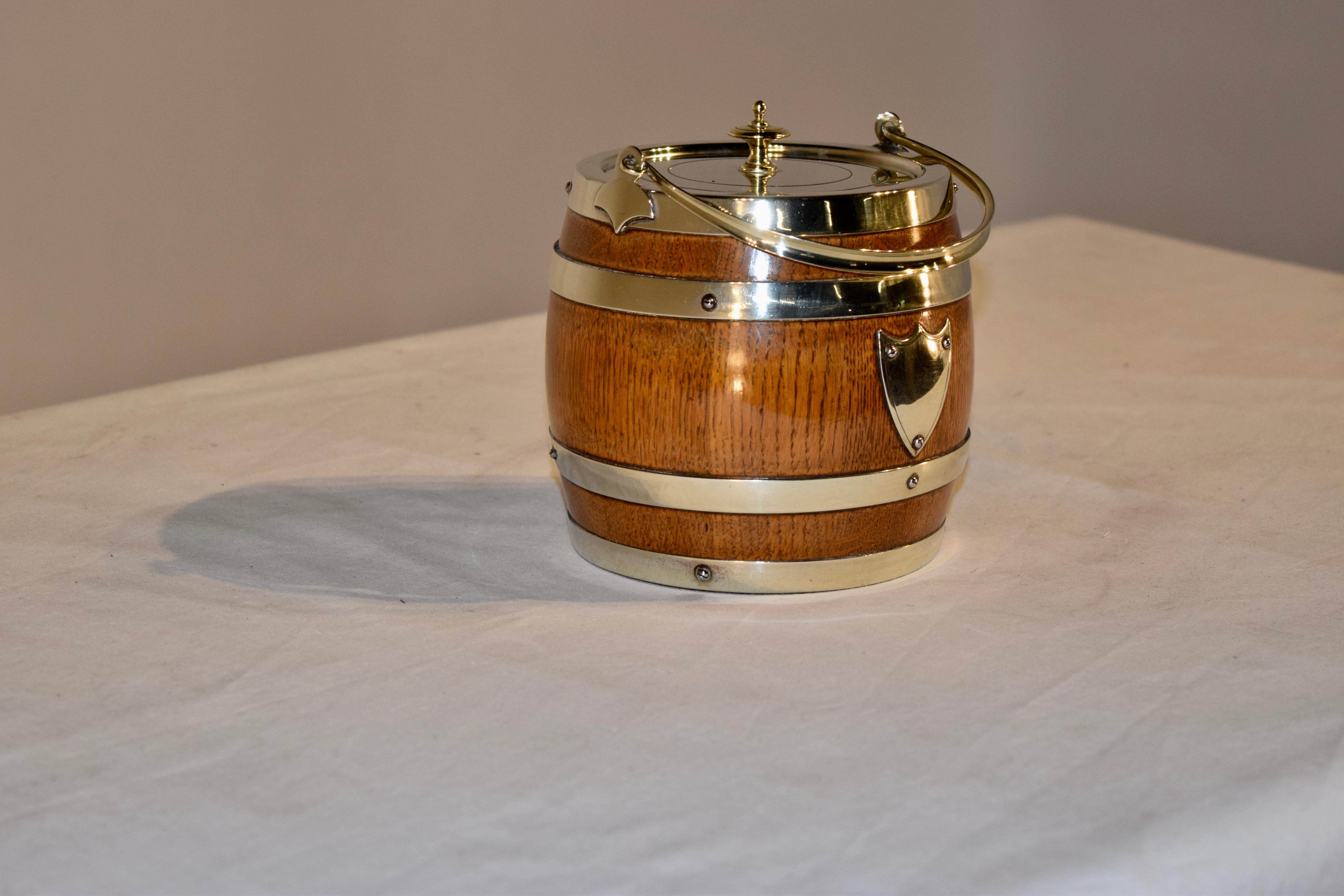 English oak biscuit barrel which retains its original porcelain liner and is banded and decorated with silver plate. Wear to silver plate from many years of polishing.