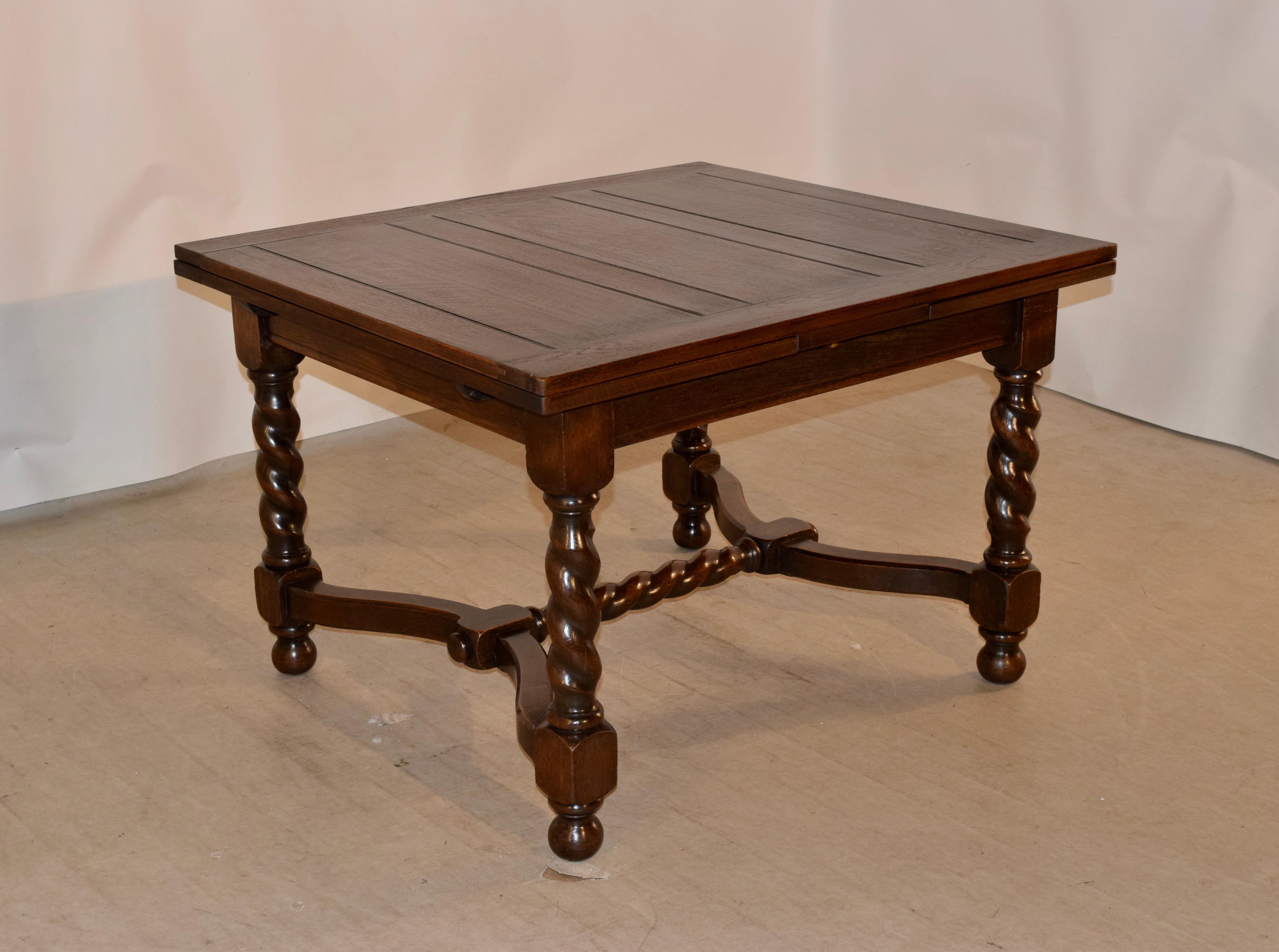 English oak draw-leaf table with a paneled top and leaves, following down to a simple apron. It is supported on hand turned barley twist legs, ending in hand turned feet and joined by serpentine stretchers and a matching hand turned barley twist