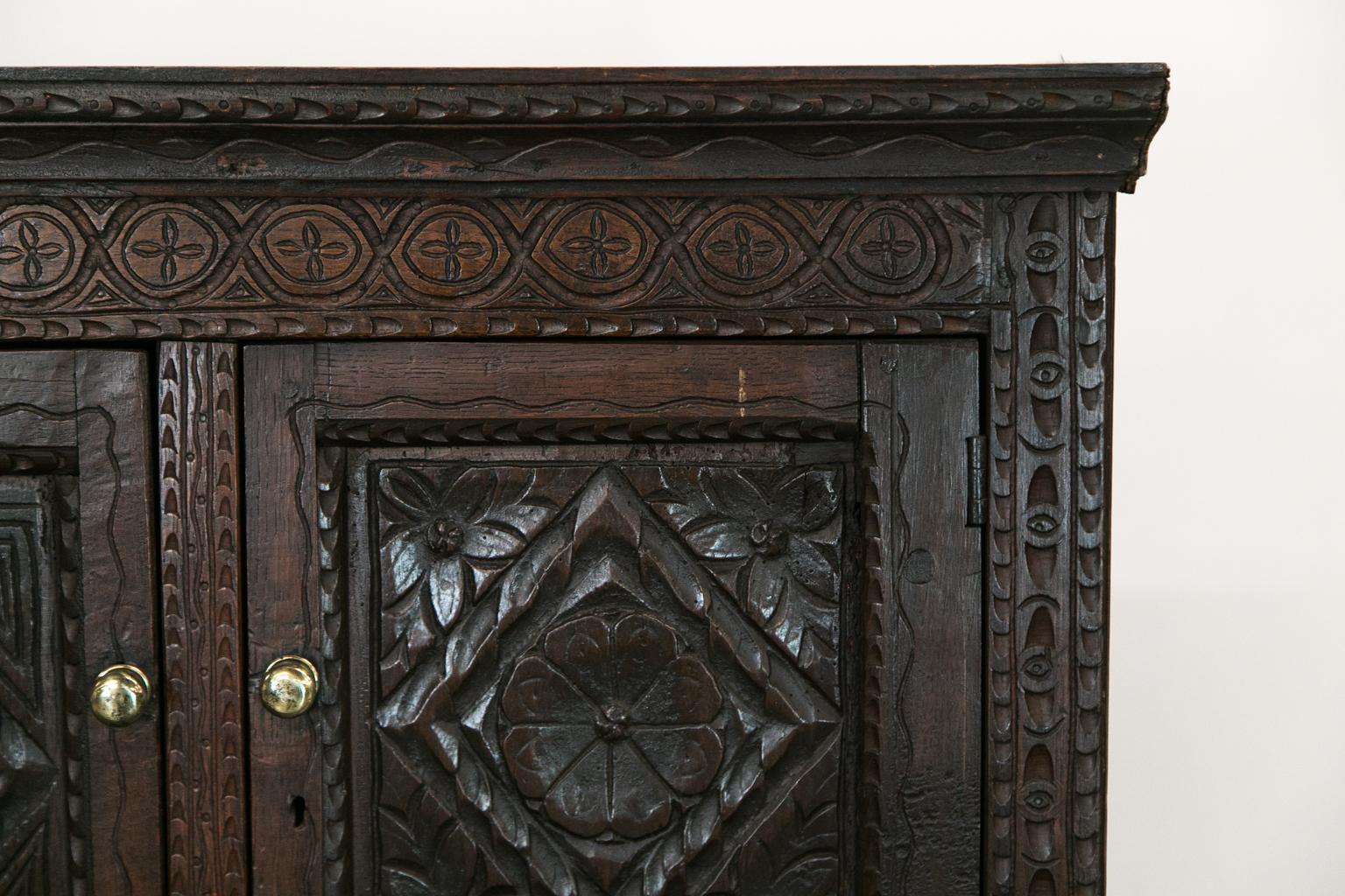 This cupboard has exposed double peg construction. It is carved overall with various floral, vine, dart, and marquee designs.