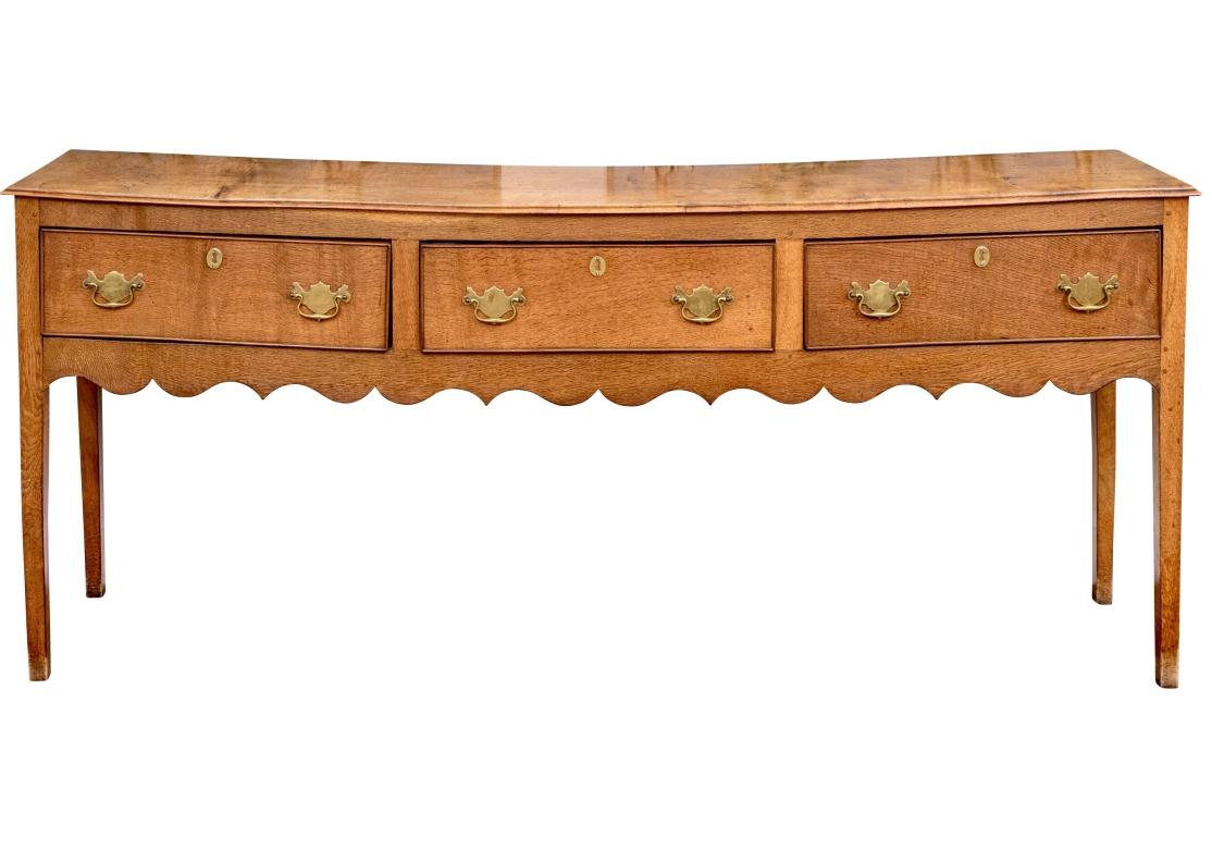 A finely crafted handsome semi antique oak sideboard. The long case with a carved edge to the top over three drawers with brass bat wing bales and faux key holes. Each drawer has traditional English quarter rounds on the inside drawer edges. A fine