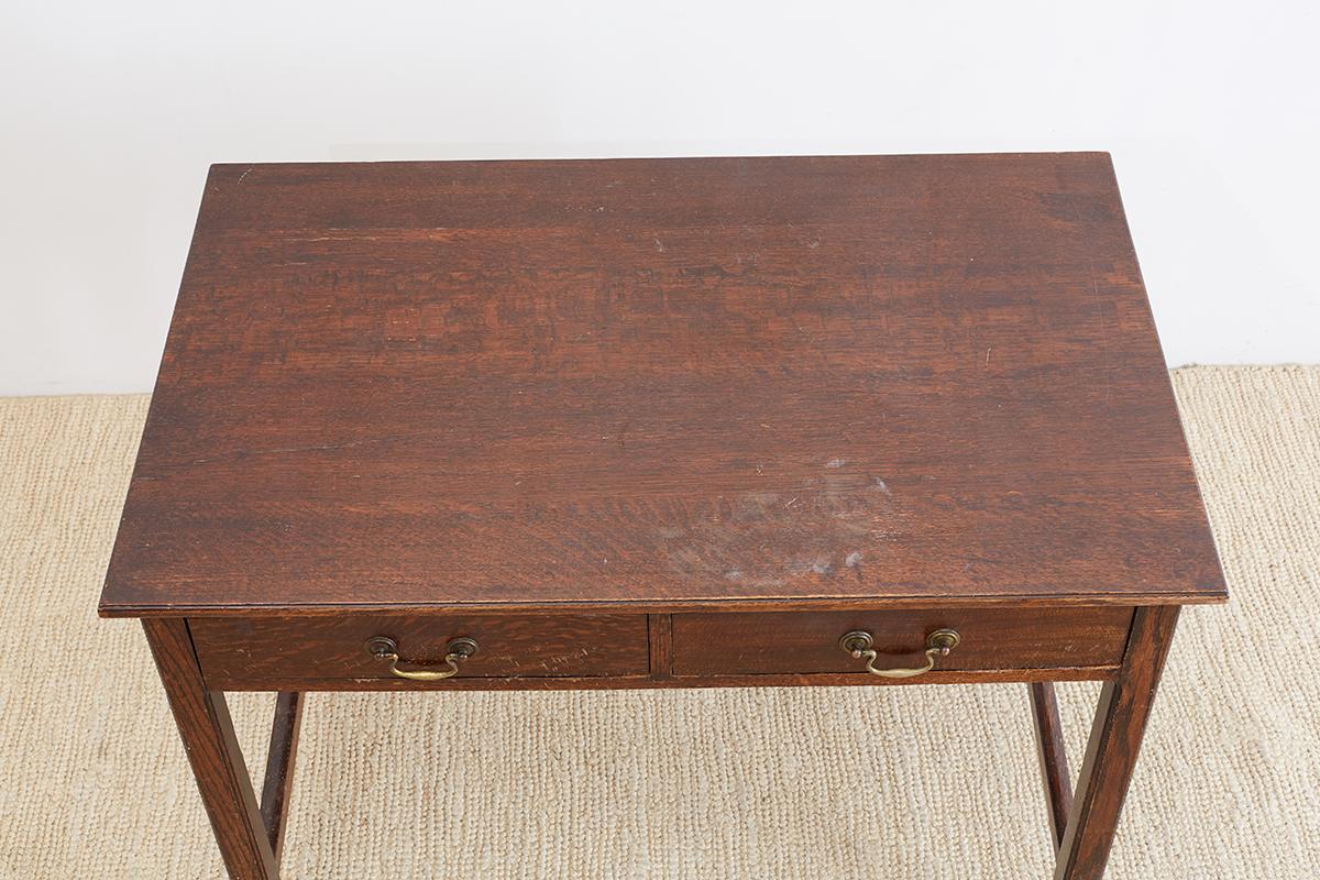 Georgian style English oak writing table or desk featuring a two drawer case. Beautifully grained oak is showcased on all sides and top. Supported by square legs with stretchers. Each drawer has brass pulls and the table is made in a simple refined