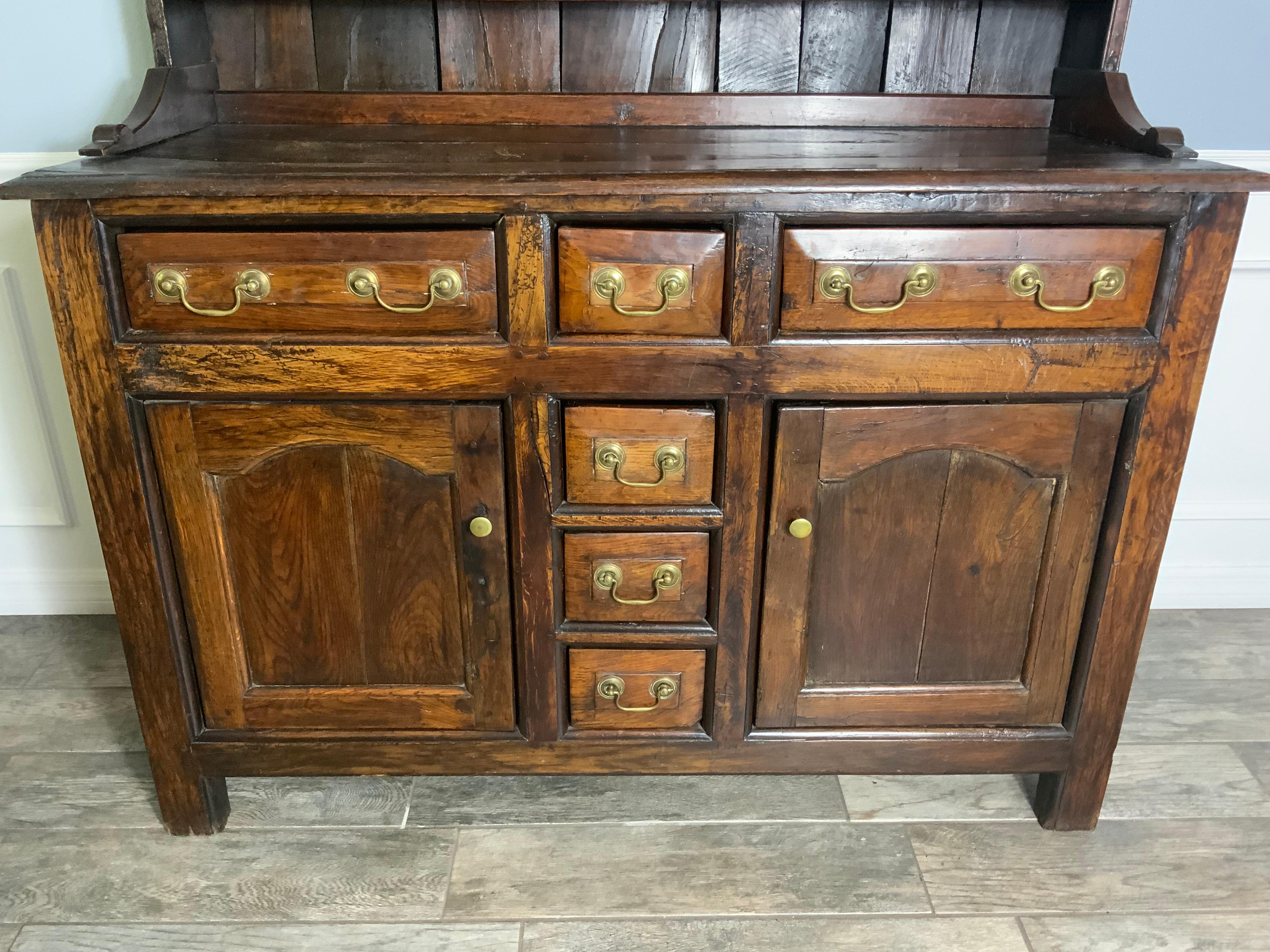A very attractive smaller size English Oak Welsh Dresser with two small cupboards in the top section and drawers and two large cupboard areas in the bottom piece.  Very nice old finish with a great color and patina.  Has had some minor repairs and
