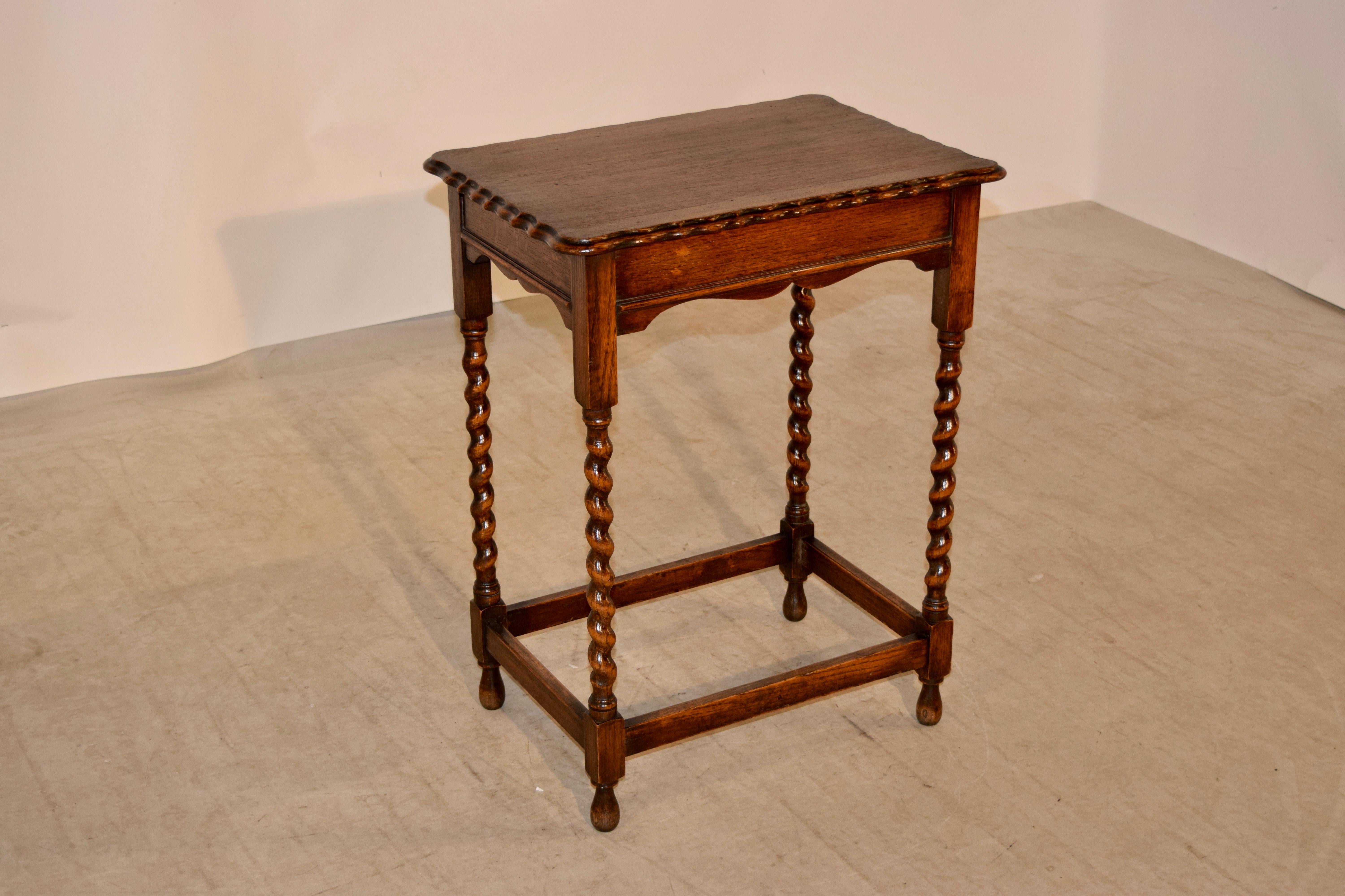 English occasional table made from oak, circa 1900. The top has a double bevelled and scalloped edge around the top following down to a scalloped apron with a molded edge. The legs are hand turned barley twist and are joined by simple stretchers and