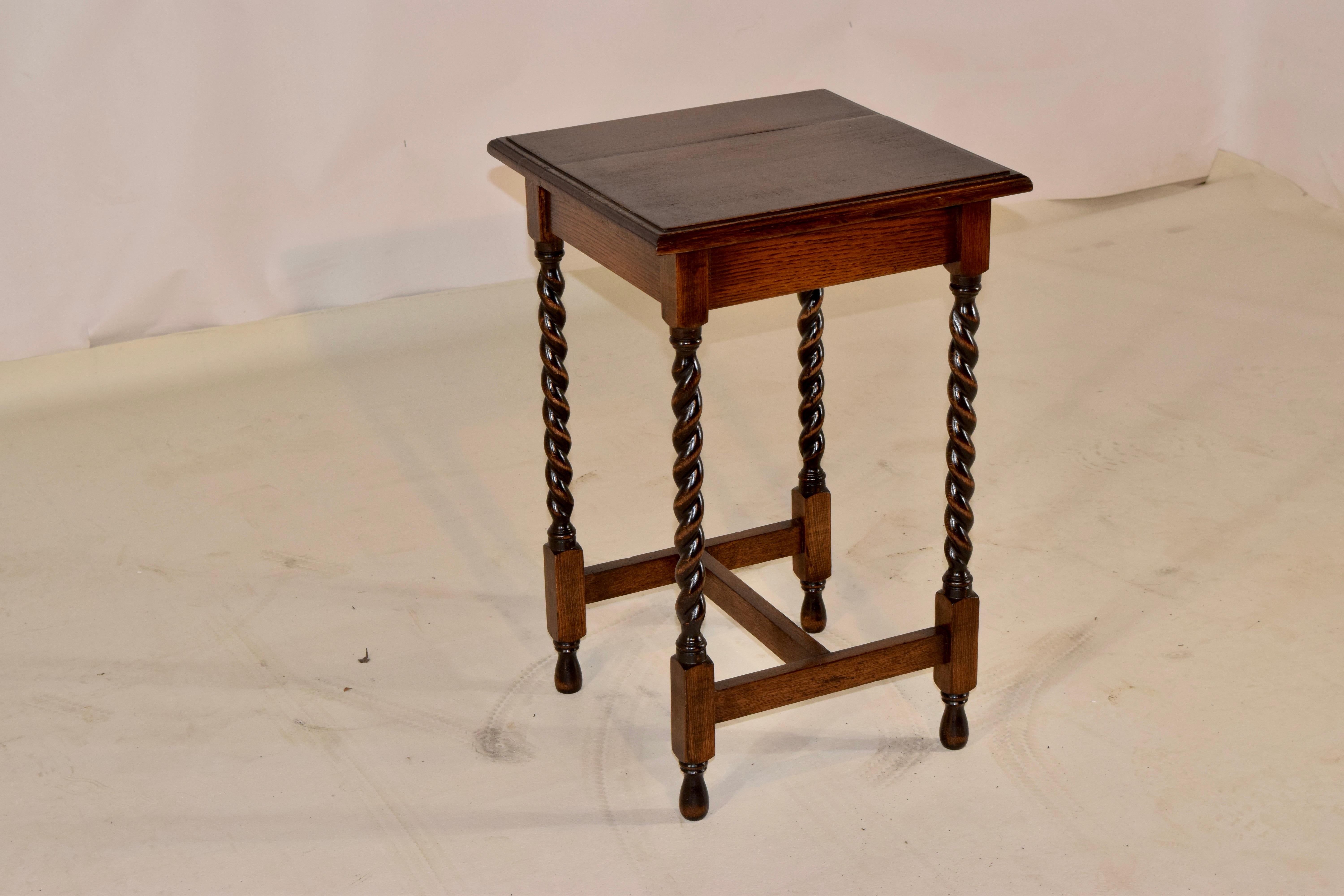 English oak occasional table with a beveled edge around the top over a simple apron and supported on hand turned barley twist legs, joined by simple cross stretchers and raised on hand turned feet.