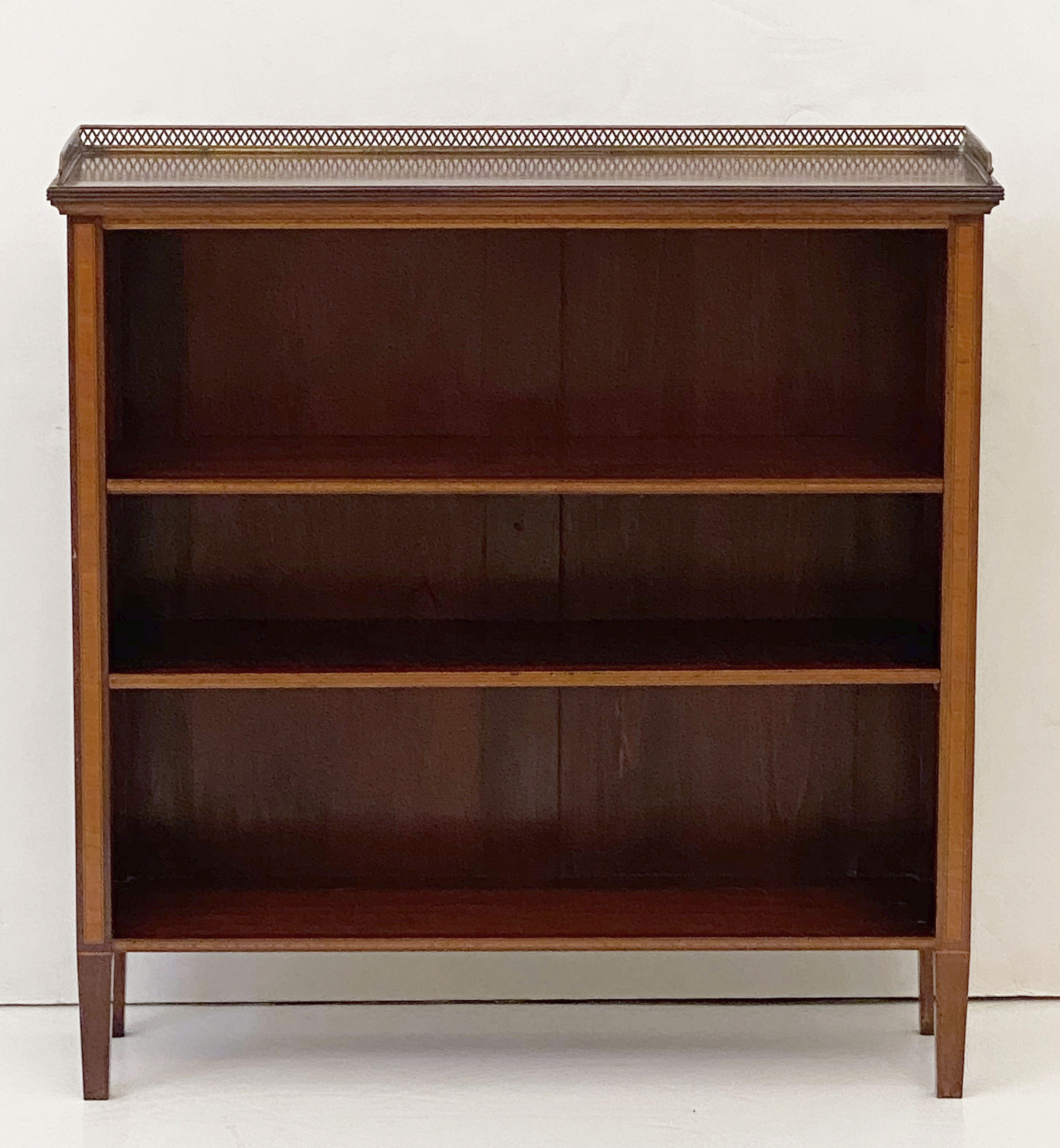 A fine English open bookcase of inlaid mahogany from the Edwardian era, featuring a moulded top with a pierced brass gallery over a frieze of two adjustable shelves and standing on four tapering feet.

With brass emblem on back: Thomas & Company,