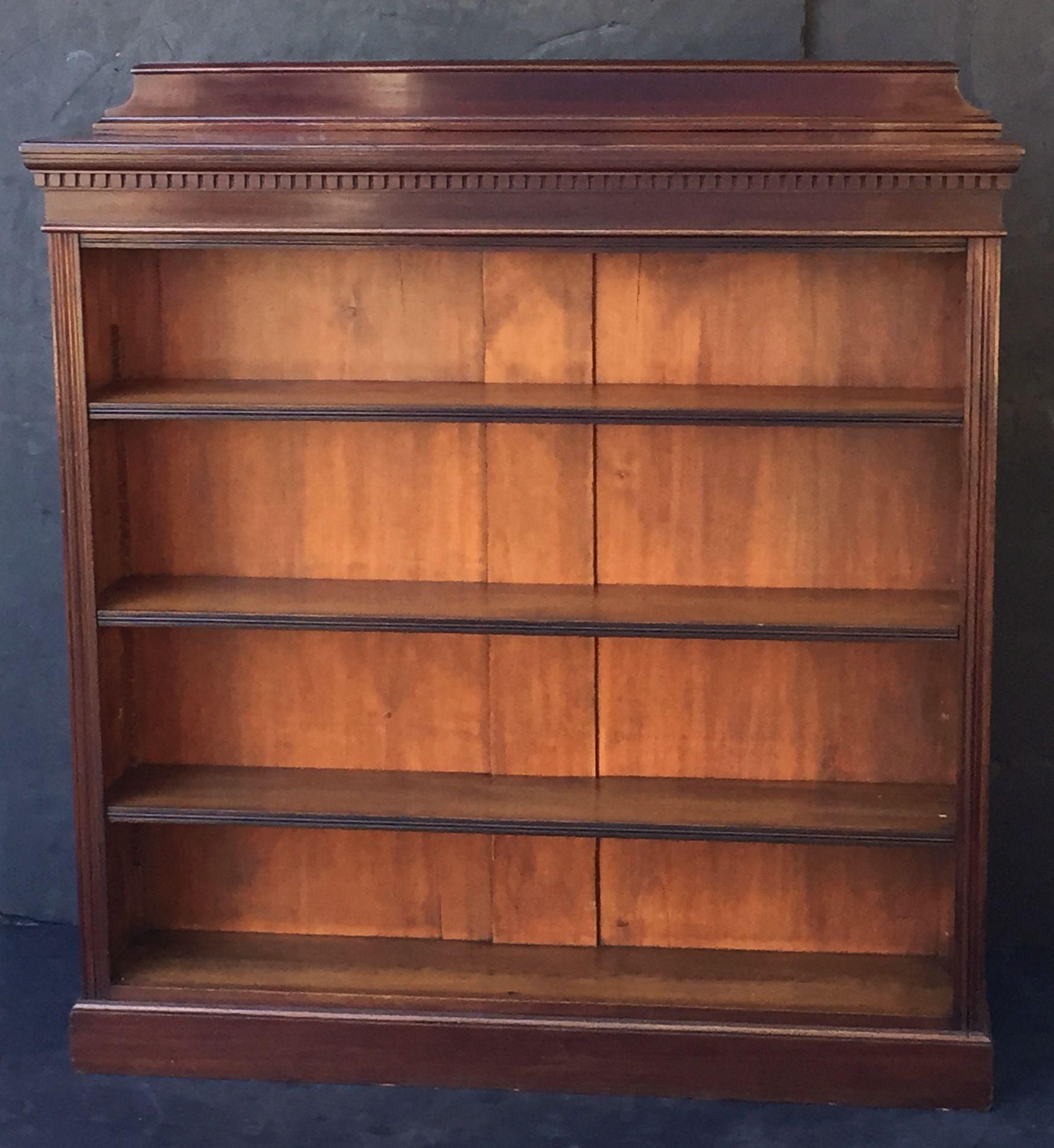 A fine English open-face bookcase of mahogany, with three adjustable shelves, featuring a moulded top and frieze with dentil trim, standing on a plinth base.