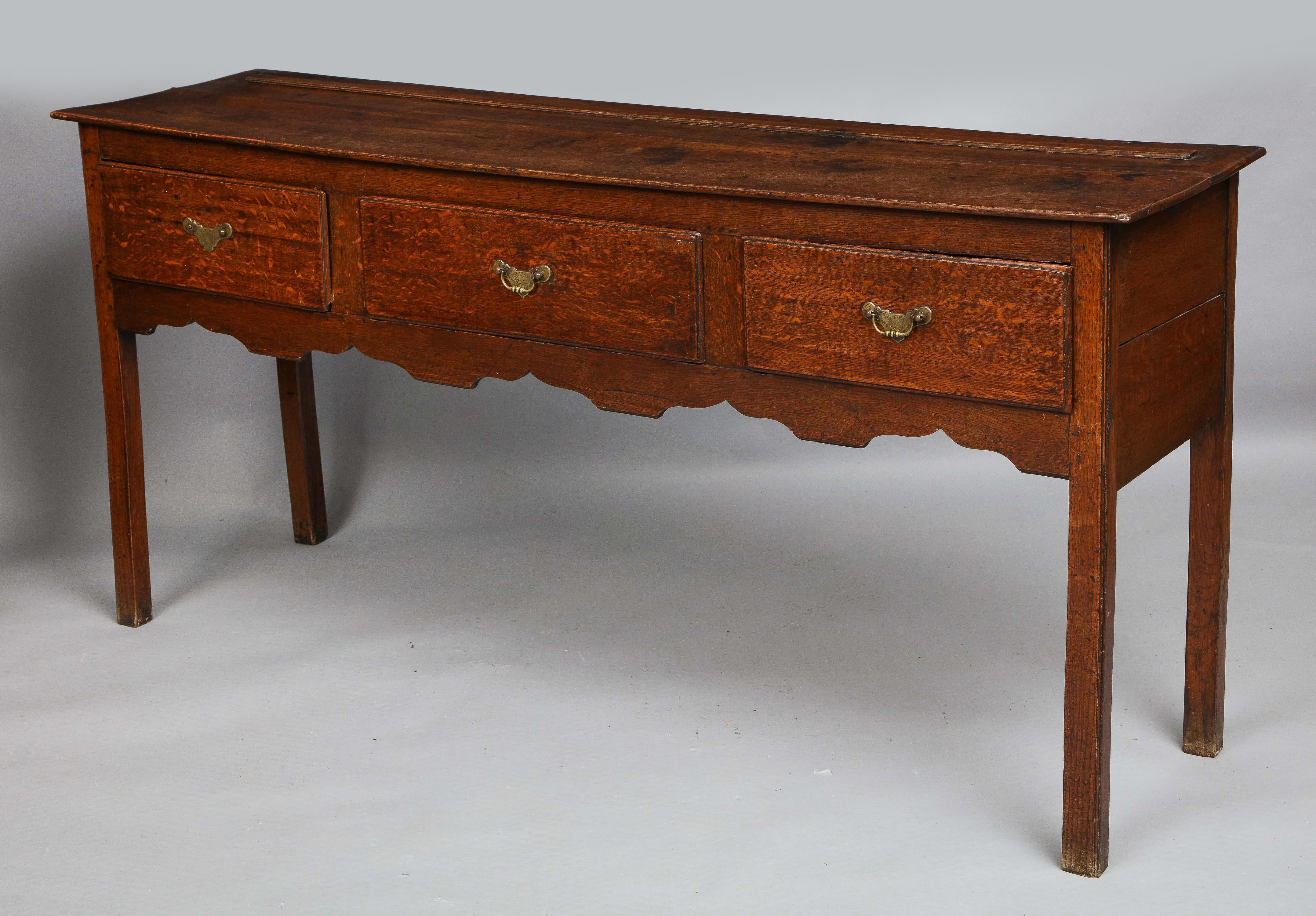 Good 18th century oak low dresser, the nicely figured top over three drawers with etched brass hardware, over lightly scalloped apron and standing on square legs with beaded outer edge, the whole with good mellow color and fine graining. The top