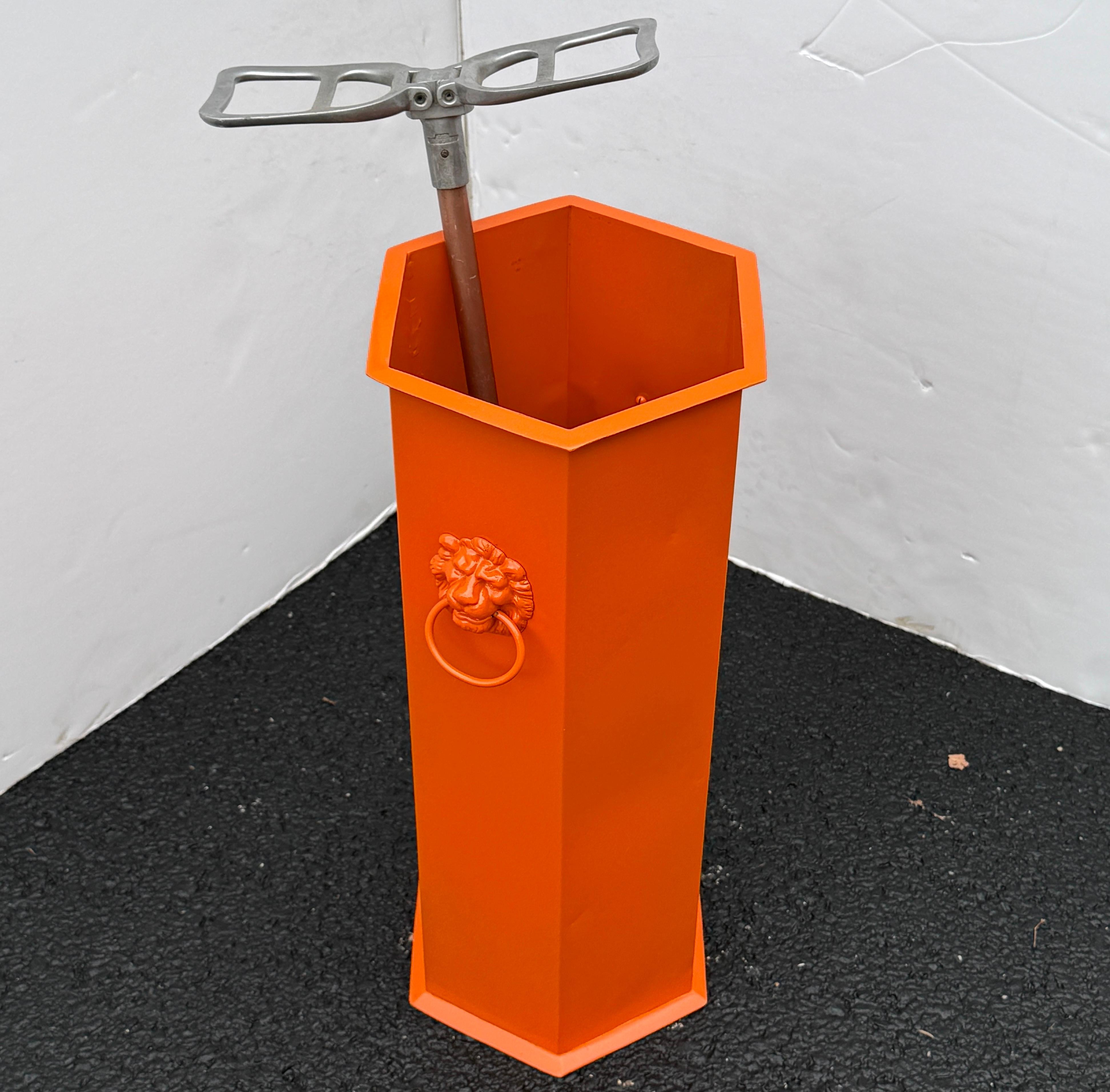 Impressionante portaombrelli o porta bastoni, circa anni '50. Lo splendido portaombrelli è stato dipinto di arancione ed è decorato con teste di leoni su ogni lato del portaombrelli. Un bellissimo pezzo funzionale da inserire in un foyer, in un