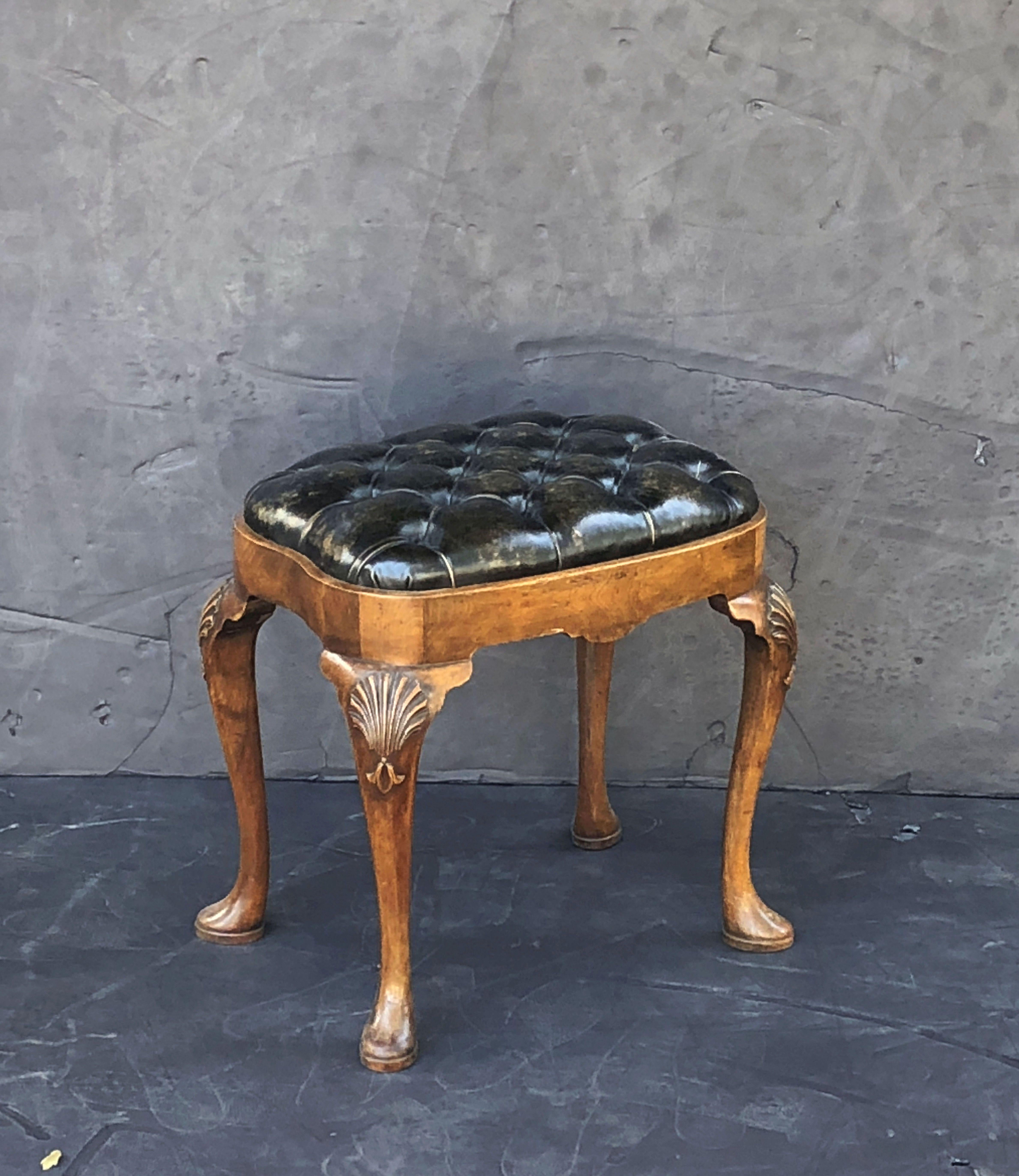 A fine English ovoid ottoman or stool, featuring a tufted black or ebony leather upholstered seat on a frame of four carved walnut cabriole legs, with shell design on each leg.