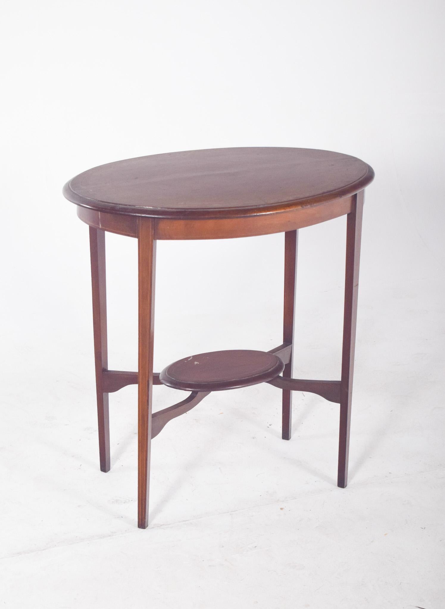 Oval side table. With an elegant and sober design, the table is made up of an oval top with slightly rounded edges, resting on four thin, straight legs. Between the legs, in the centre, is a shelf that is also oval, serving as extra support or for