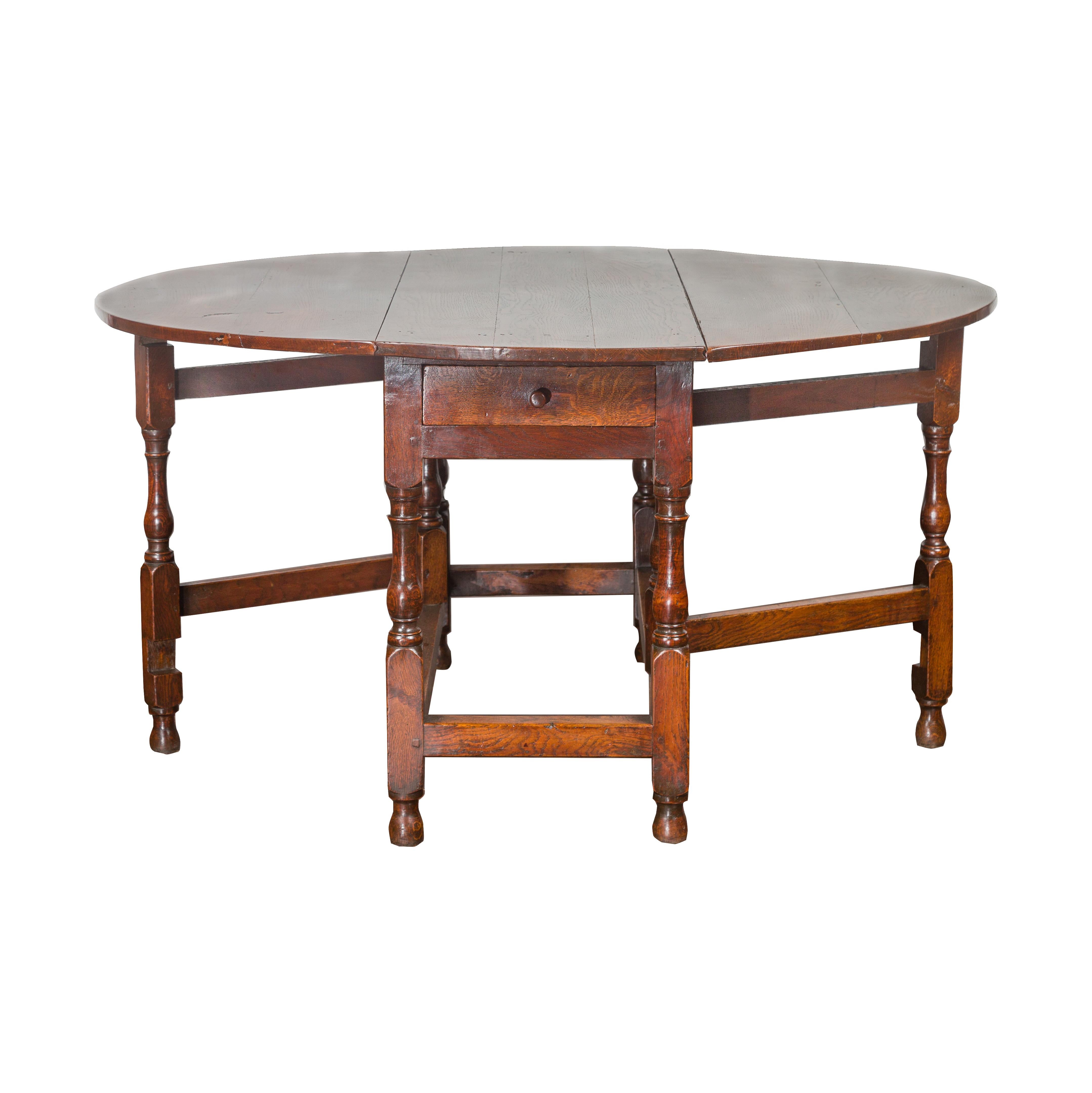 Table ovale à abattant en chêne anglais de la fin du XIXe siècle, avec un seul tiroir et des pieds balustres. Créée en Angleterre au cours du troisième quart du XIXe siècle, cette table en chêne présente un plateau ovale composé de deux feuilles