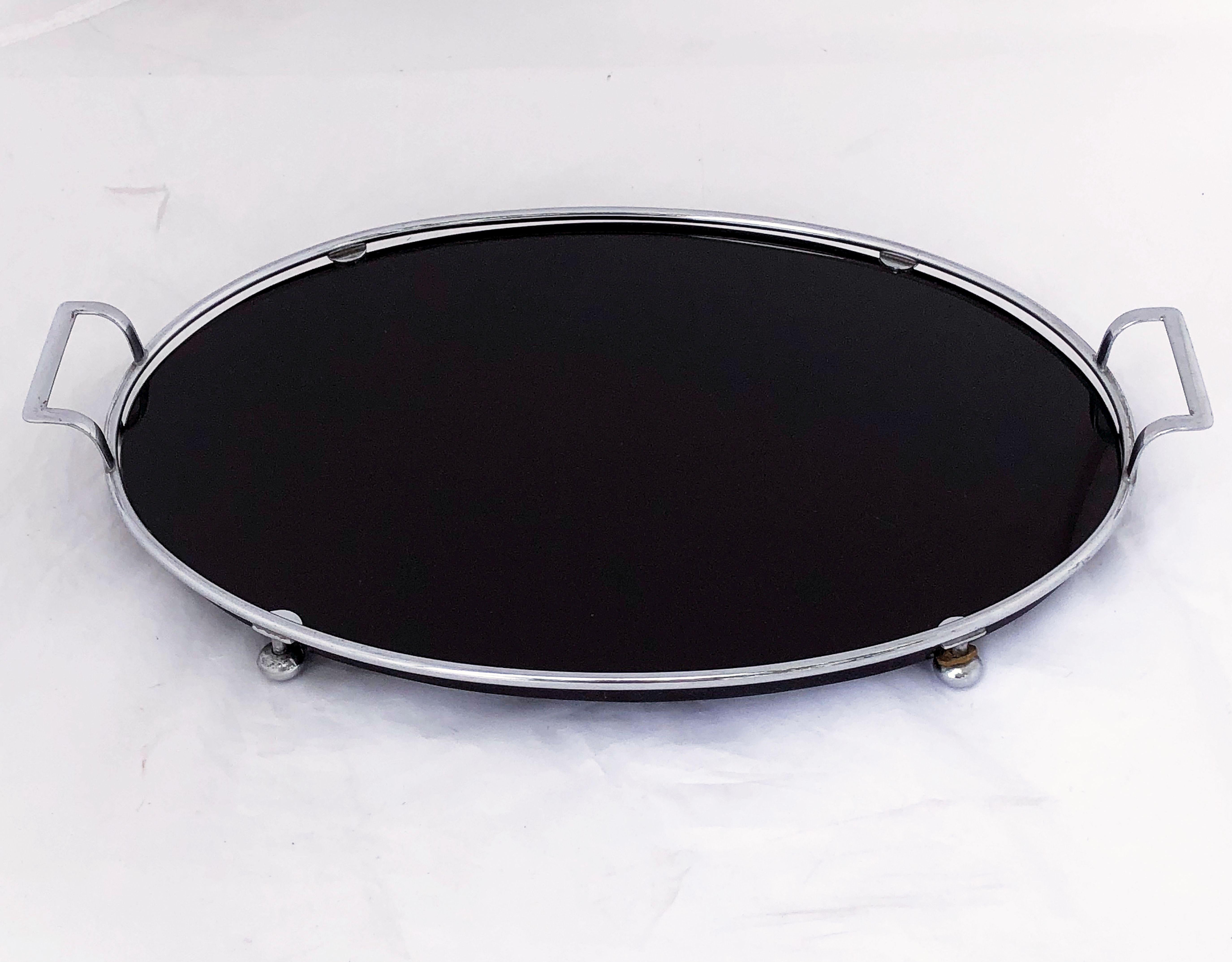 A fine English oval serving tray from the Art Deco period, featuring an oval black or ebony glass mounted to a stylish chrome metal frame with opposing handles and round feet (with two original rubber washers).