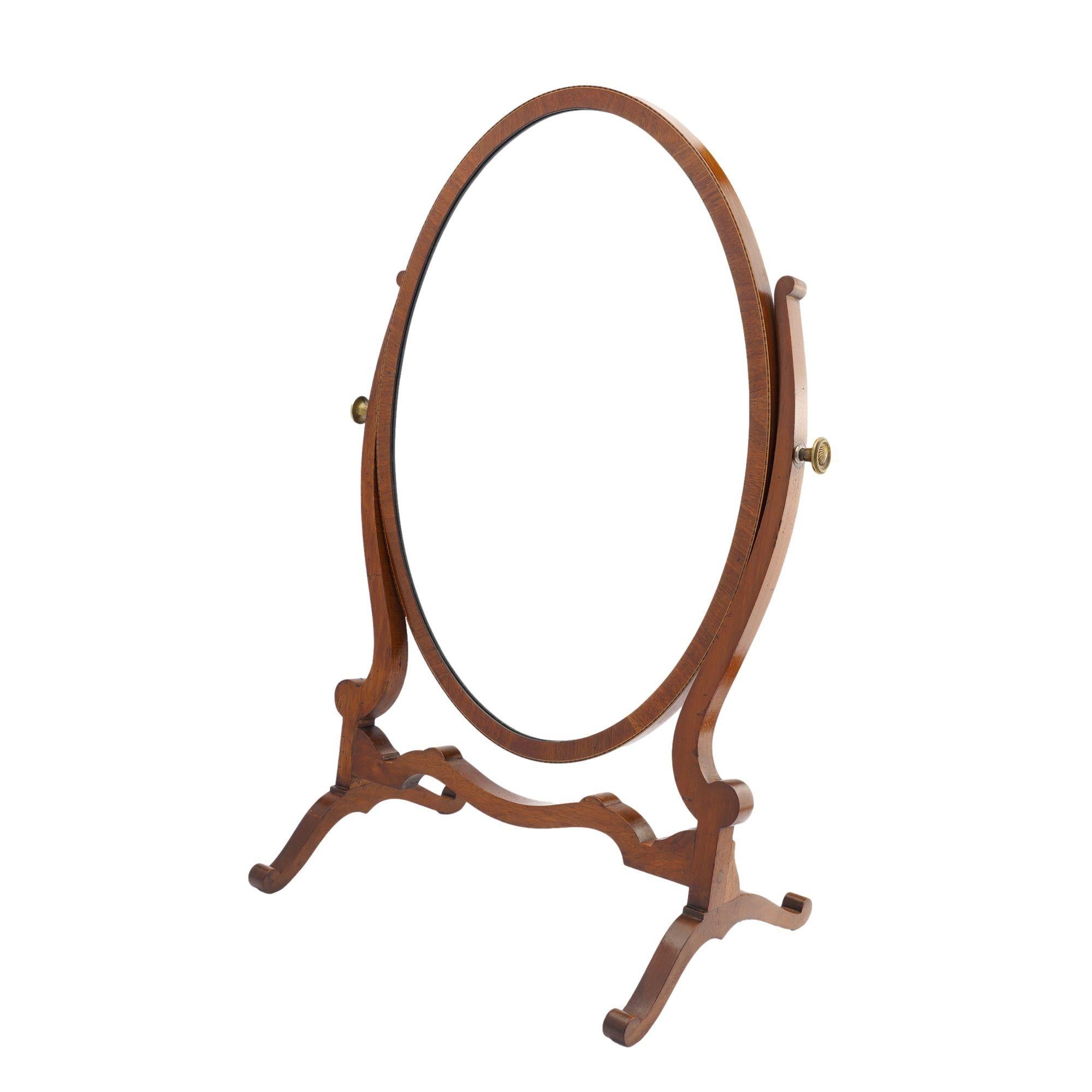 Oval tabletop swinger mirror in mahogany with delicate stringing around the mirror frame. Mirror is mounted on a sculptural mahogany stand with brass tilter knobs. 
England, 1800-25.