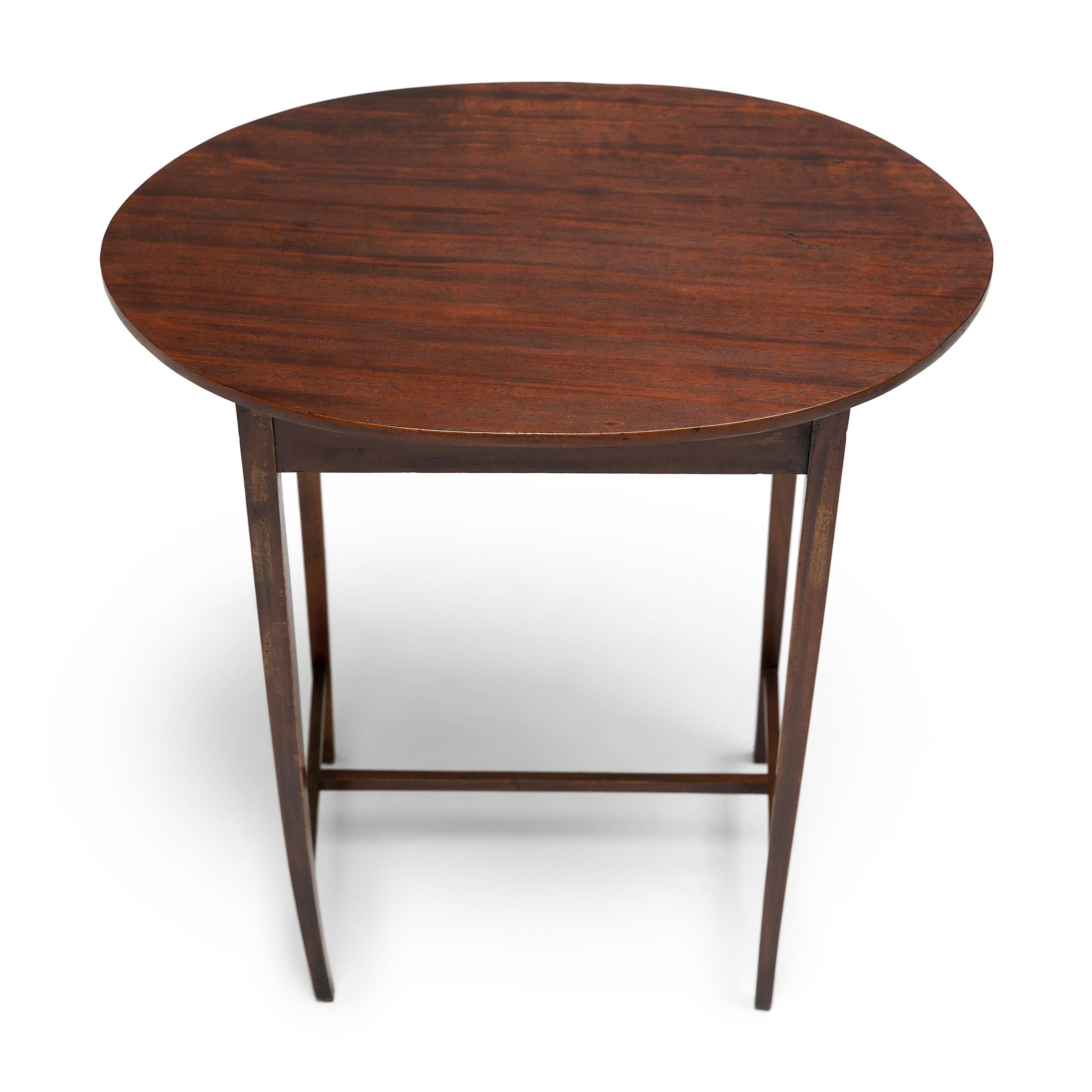 This antique English side table is elegantly crafted with a versatile and lightweight design. Recently refinished to a rich, dark brown, the small table features an oval top resting on four narrow legs linked with straight stretchers. Recalling