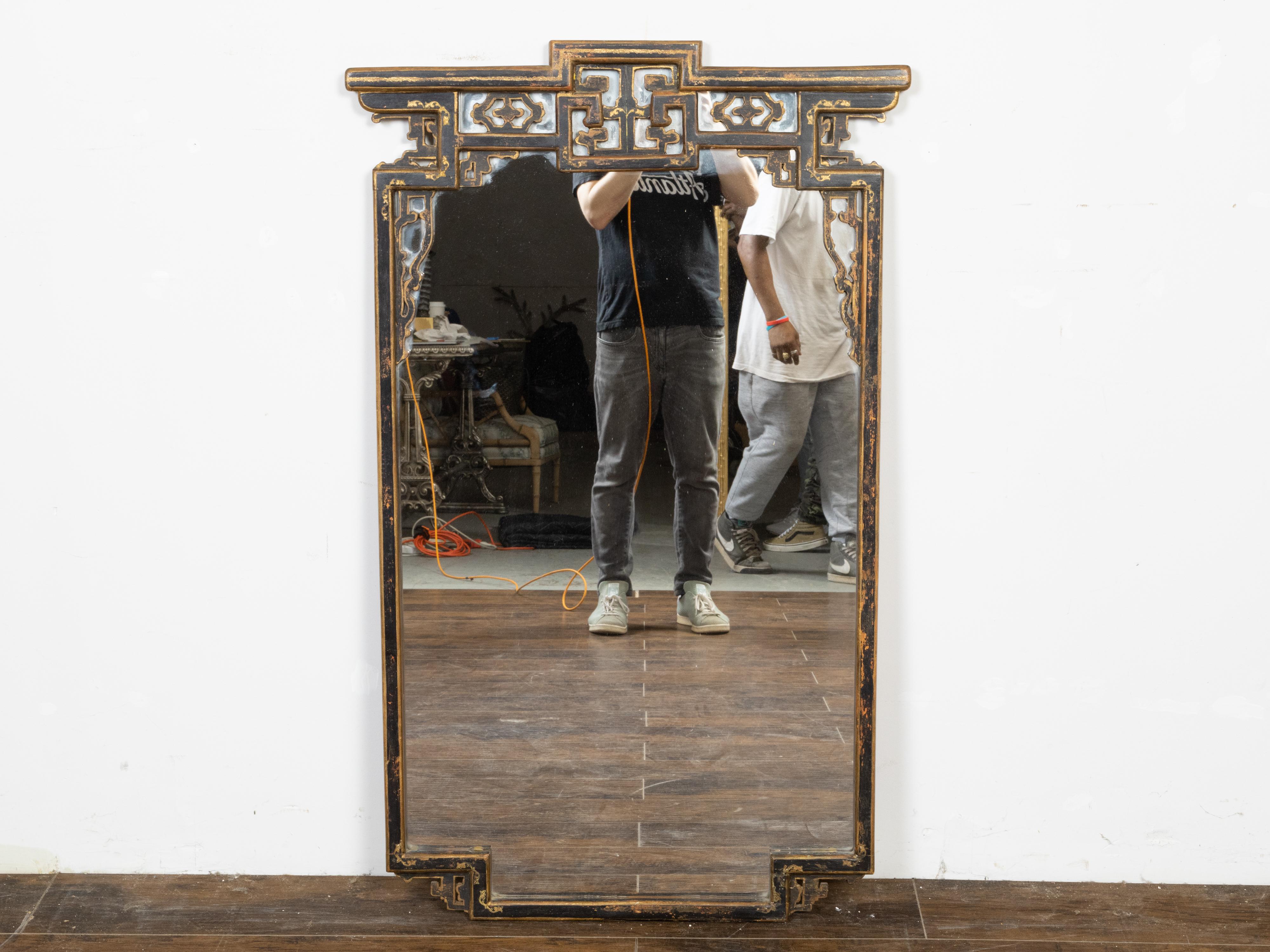An English painted wall mirror from the mid 20th century, with carved openwork motifs, black and golden tones and distressed finish. Created in England during the second quarter of the 20th century, this wall mirror attracts the attention with its