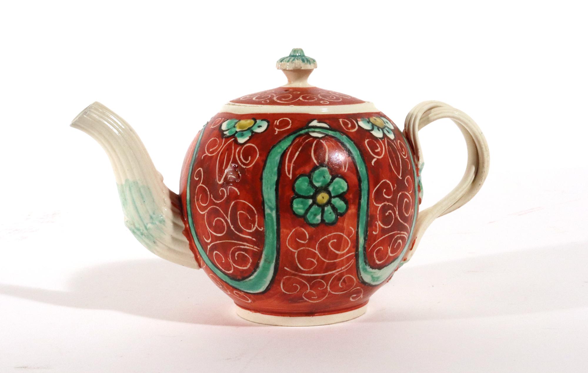 English Painted Orange-ground Creamware Teapot and Cover,
Circa 1780

The rust-orange ground has incised markings to imitate leaves for the green and yellow flower heads found between a looping green enamel ribbon.  There is some small loss to the