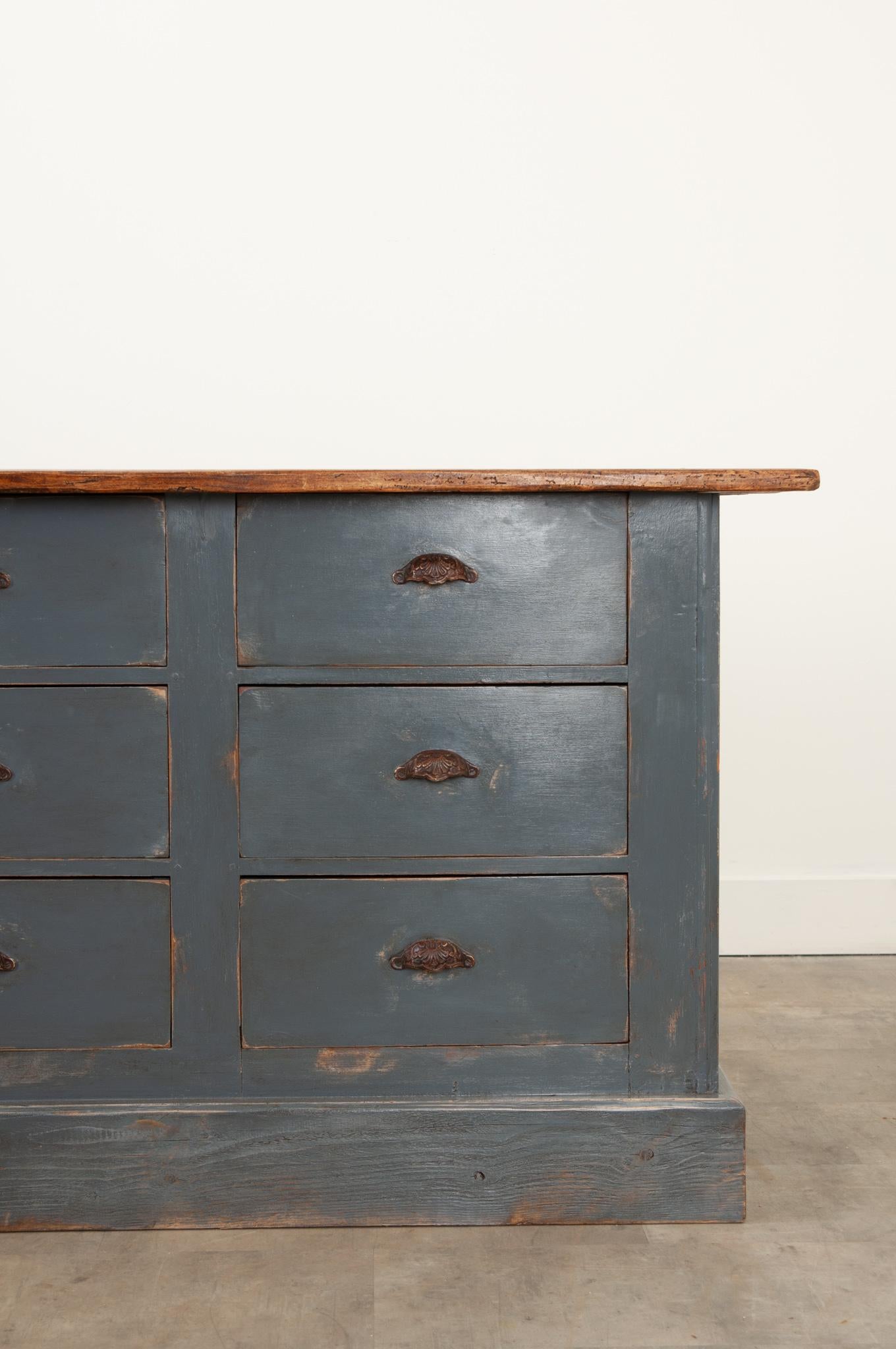 A large pine shop counter, sourced from a haberdasher in England. The counter dates to 1870 and has had a long career as a fully functional organizational case piece. The affixed countertop is made of three long boards of pine that showcase its rich