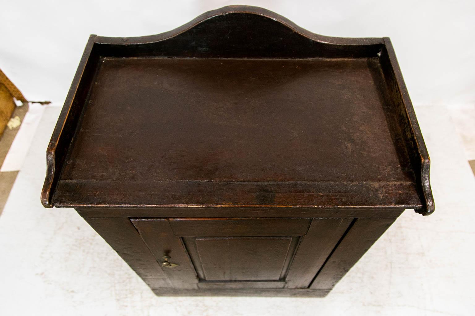 The top of this washstand has a shaped gallery on three sides. The door has a raised panel. There are small shrinkage separations in the top door and sides. The paint has wear and crazing commensurate with use and age. The interior has one fixed