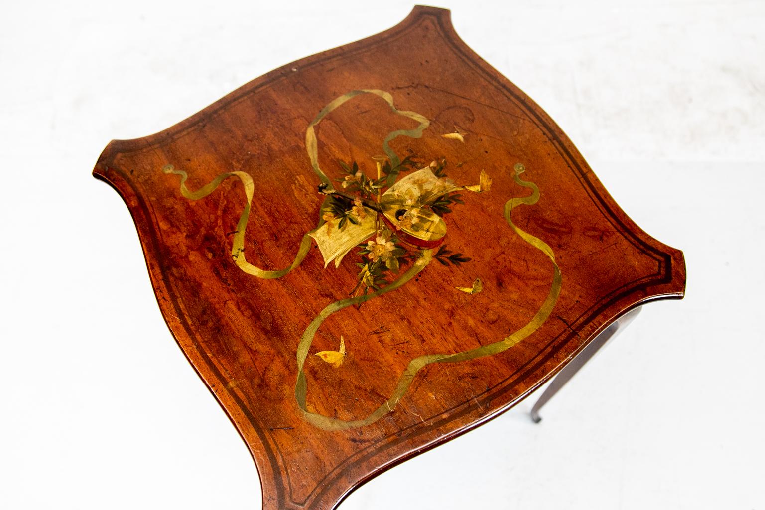 English painted satinwood occasional table, the top with serpentine sides and painted inlay border surrounding a musical theme cartouche with mandolin music score and brass horns. The cartouche is surrounded by flowing ribbon, flowers, and